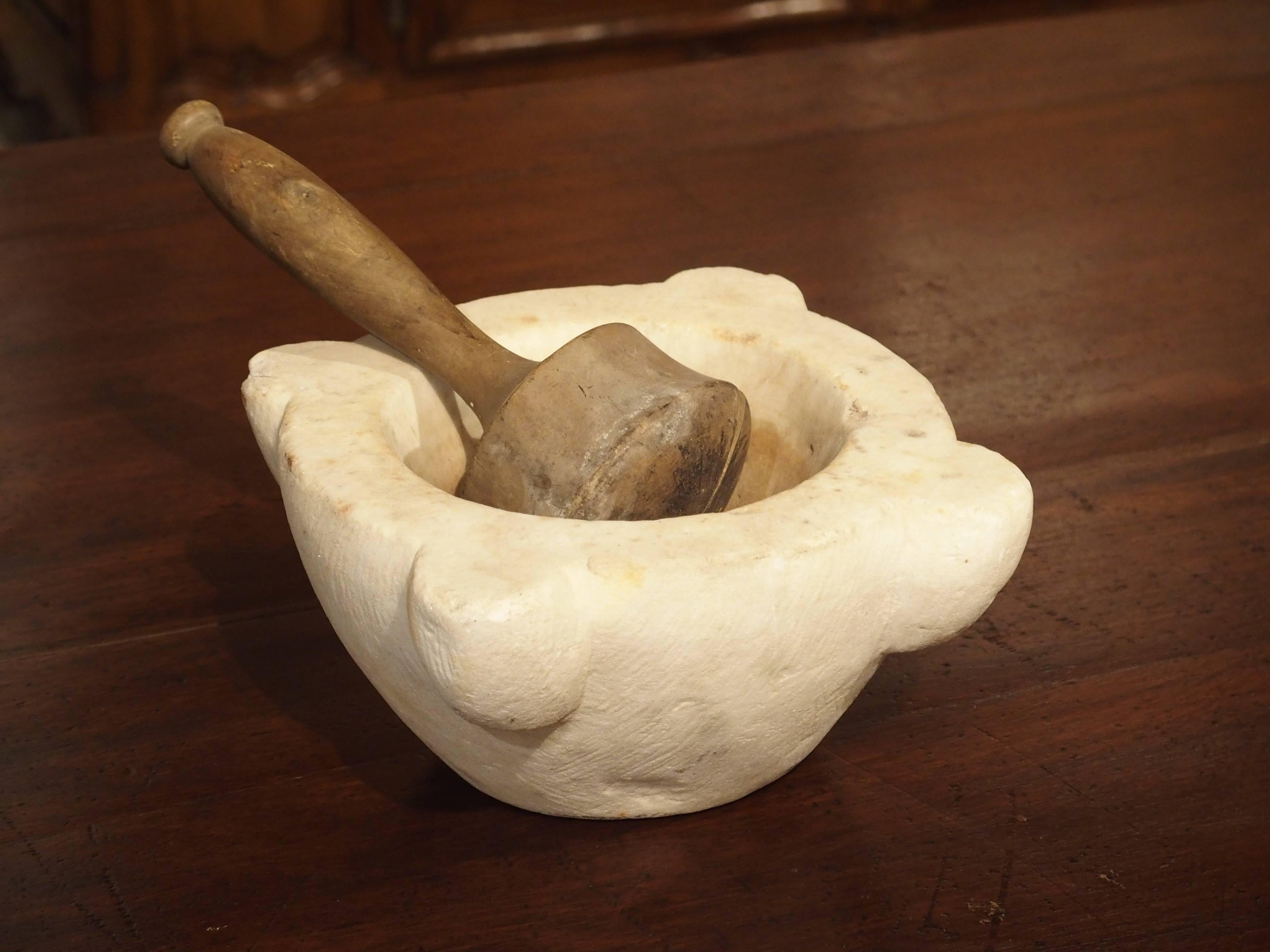 This small marble mortar and wooden pestle is from France and dates to the 19th century. It is made from a cream colored marble and has four out turned motifs. The wooden pestle has a flat bottom.

 In France, these were used in the kitchens of