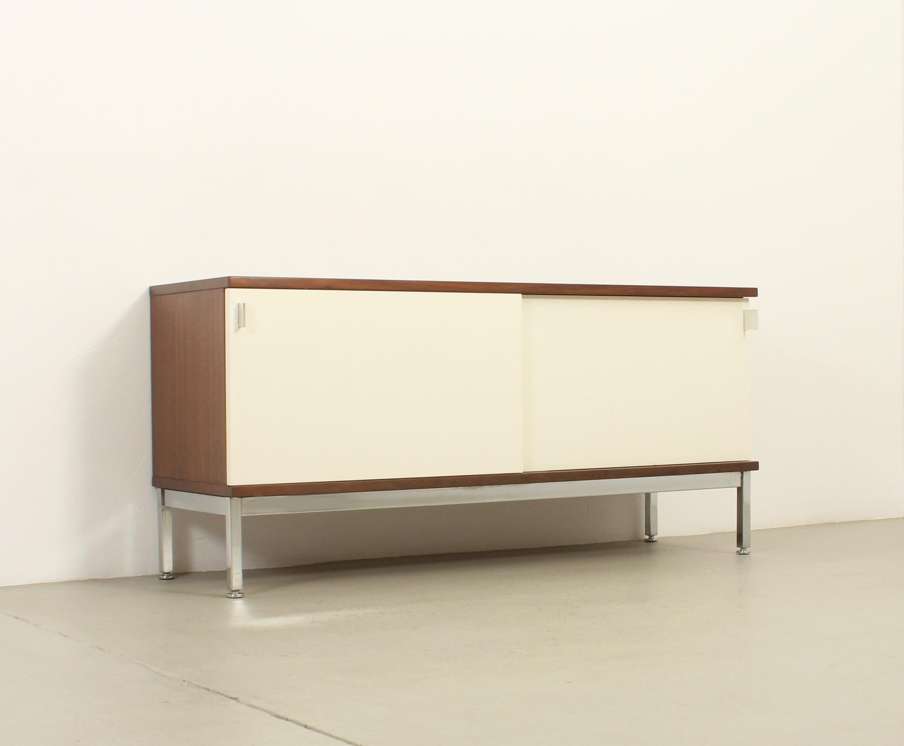 Piccola credenza edita negli anni '60 da Airborne, Francia. Legno di betulla con due ante scorrevoli laccate bianche con base in acciaio cromato e maniglie in alluminio lucido. Due spazi con un ripiano interno. Vedi l'altra credenza piccola per una