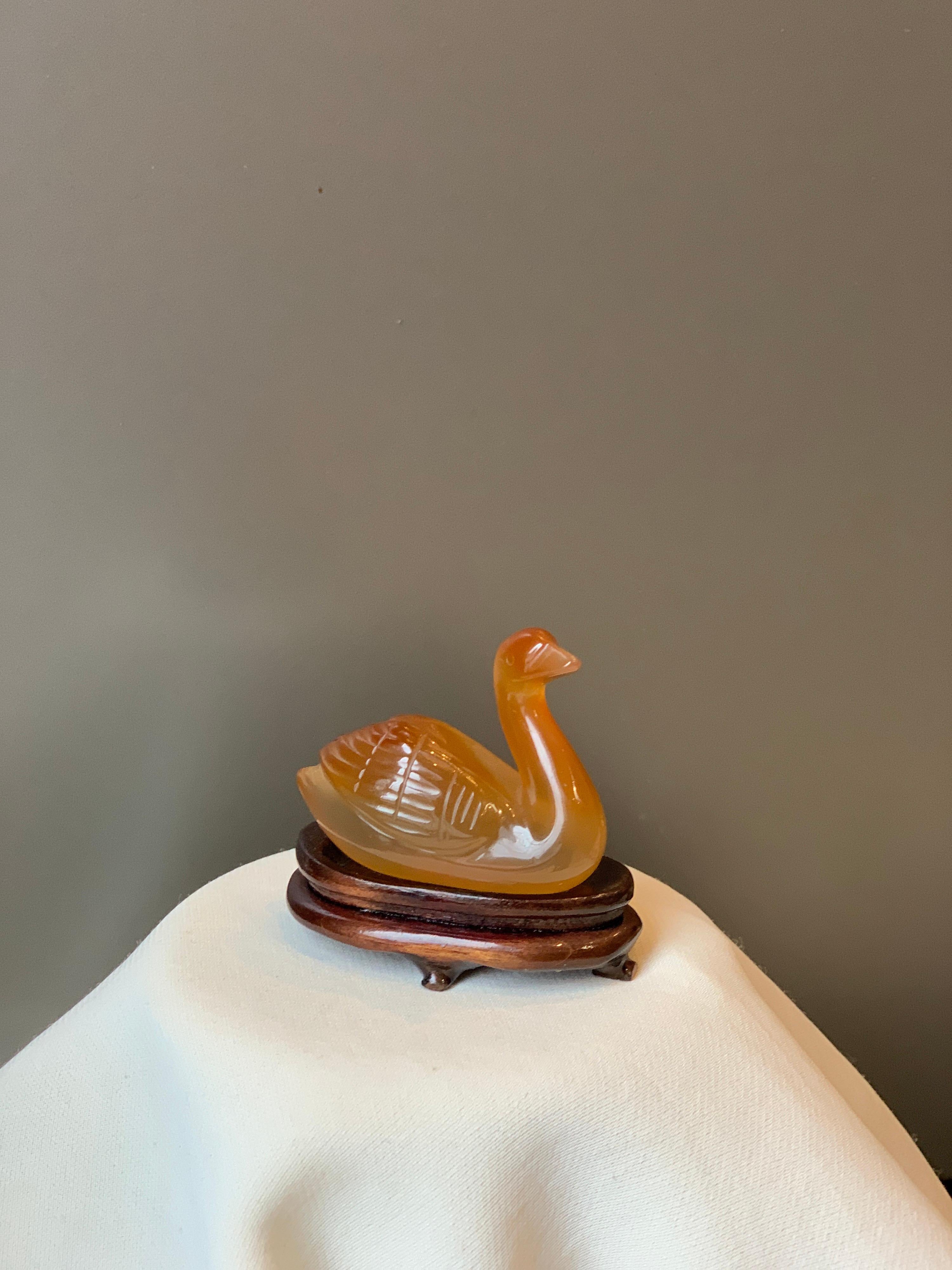 Small Amber Chinese decorative swan on a wooden stand.
