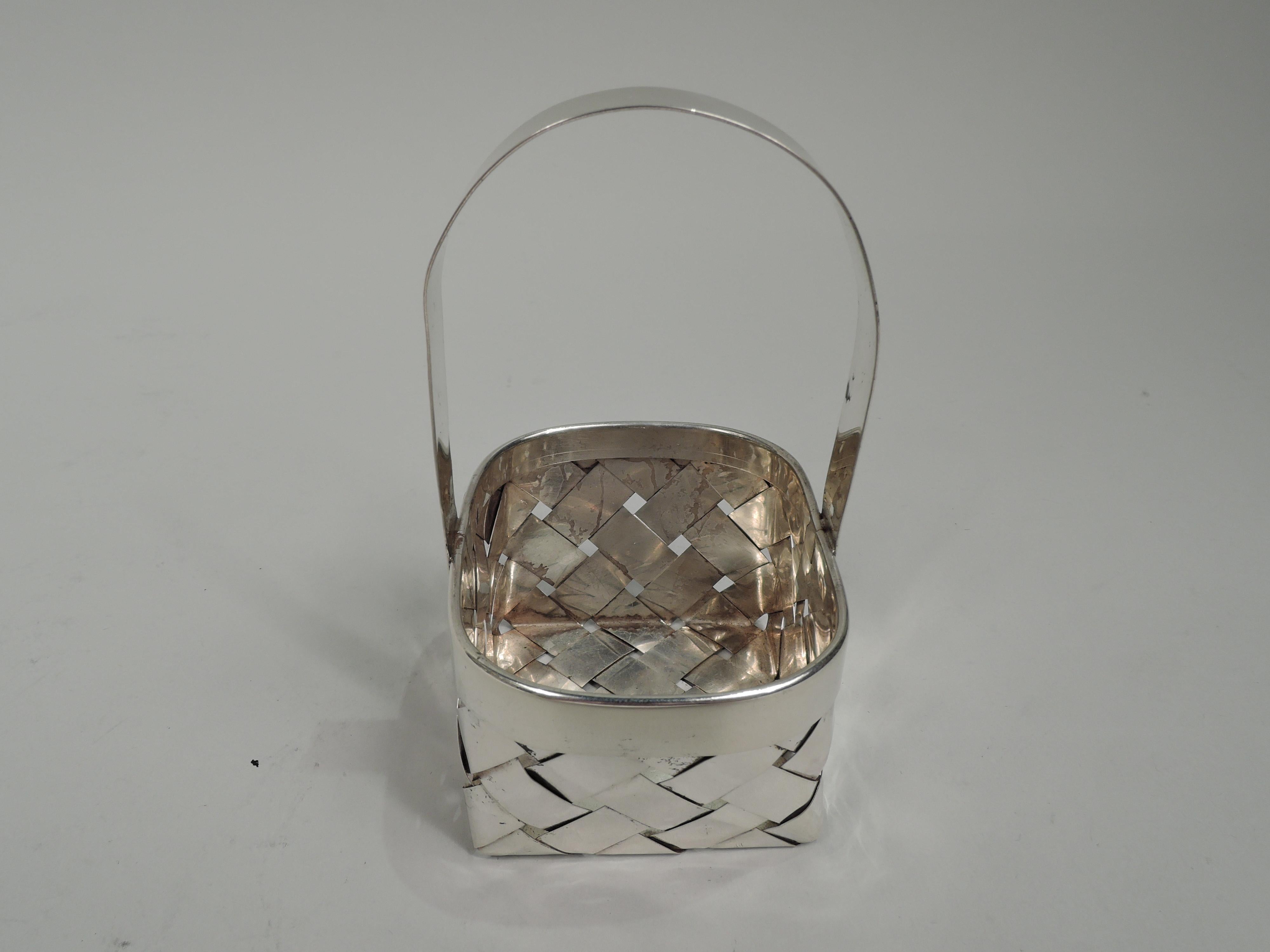 American Mid-Century Modern sterling silver basket. Rectangular with straight sides and curved ends. Plain rim and fixed and high c-scroll handle. Woven strips. Marked “Sterling”. Weight: 1.6 troy ounces.