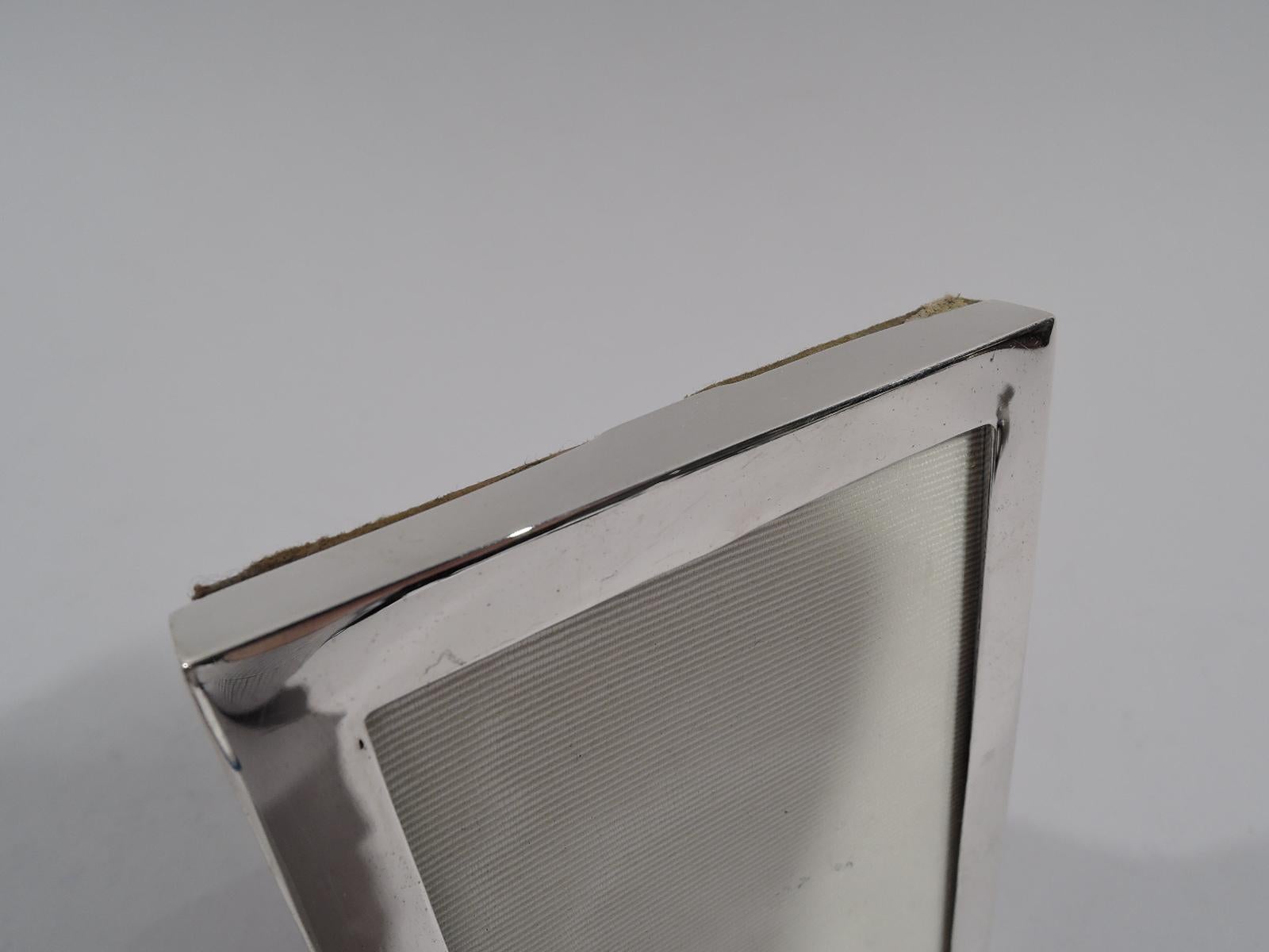 Small modern sterling silver picture frame. Made by Gorham in Providence, circa 1920. Rectangular window in plain flat surround. With glass, silk lining, and velvet back and hinged support for portrait (vertical) display. Fully marked and numbered