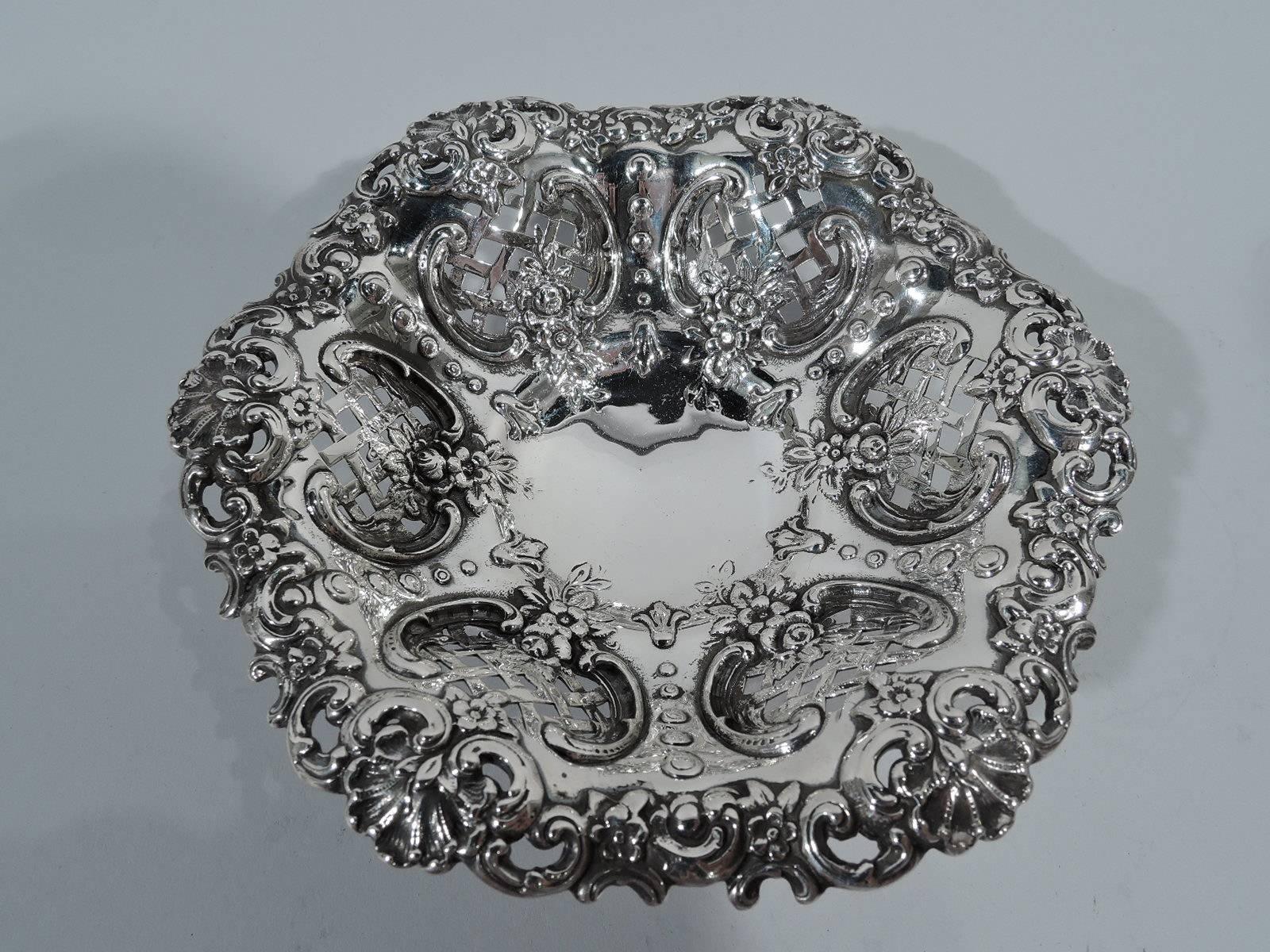 Small and sumptuous sterling silver bowl. Made by Tiffany & Co. in New York. Circular plain well, tapering and lobed sides, and wavy rim. Sides interior have scrolled frames with pierced diaper pattern and flowers. Rim has c-scrolls, scallop shells,
