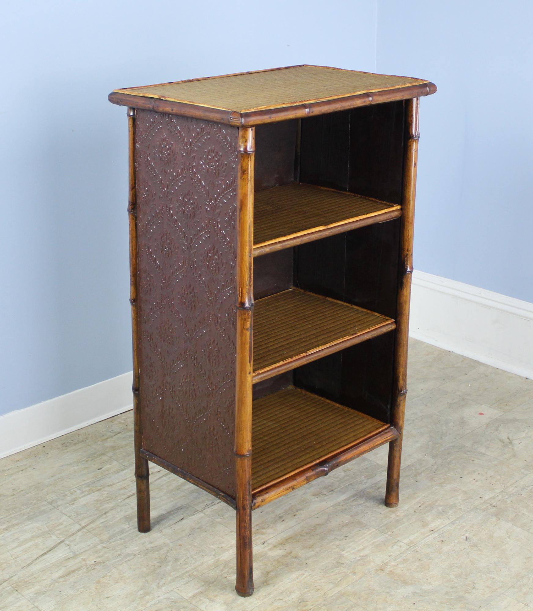 A charming Victorian bamboo bookcase from England. The rattan on top is original, as is the pressed leather on the sides of the piece and the rattan on the interior shelves. This piece is in very god condition for its age. Fun and useful!