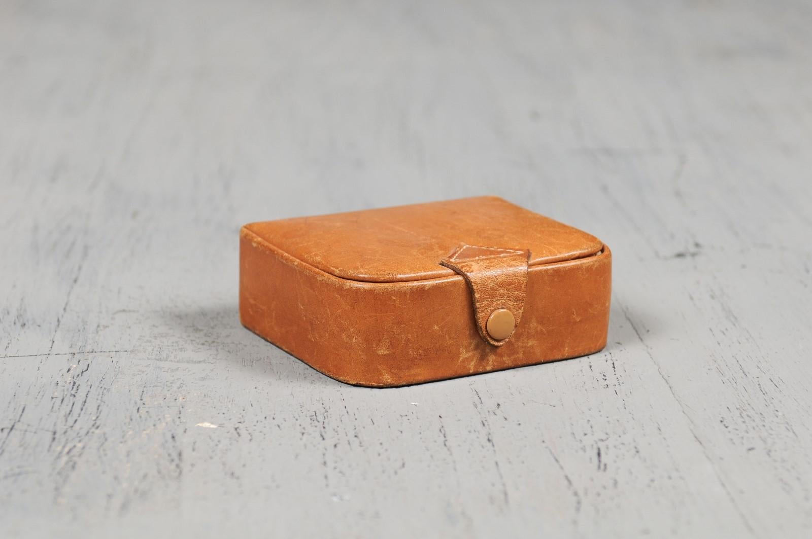 A small antique Camalier & Buckley leather case from the 20th century with buttoned strap. Founded in the 1930s in the United States, Camalier & Buckley produced this handsome leather case boasting a caramel color and a small buttoned strap. Perfect