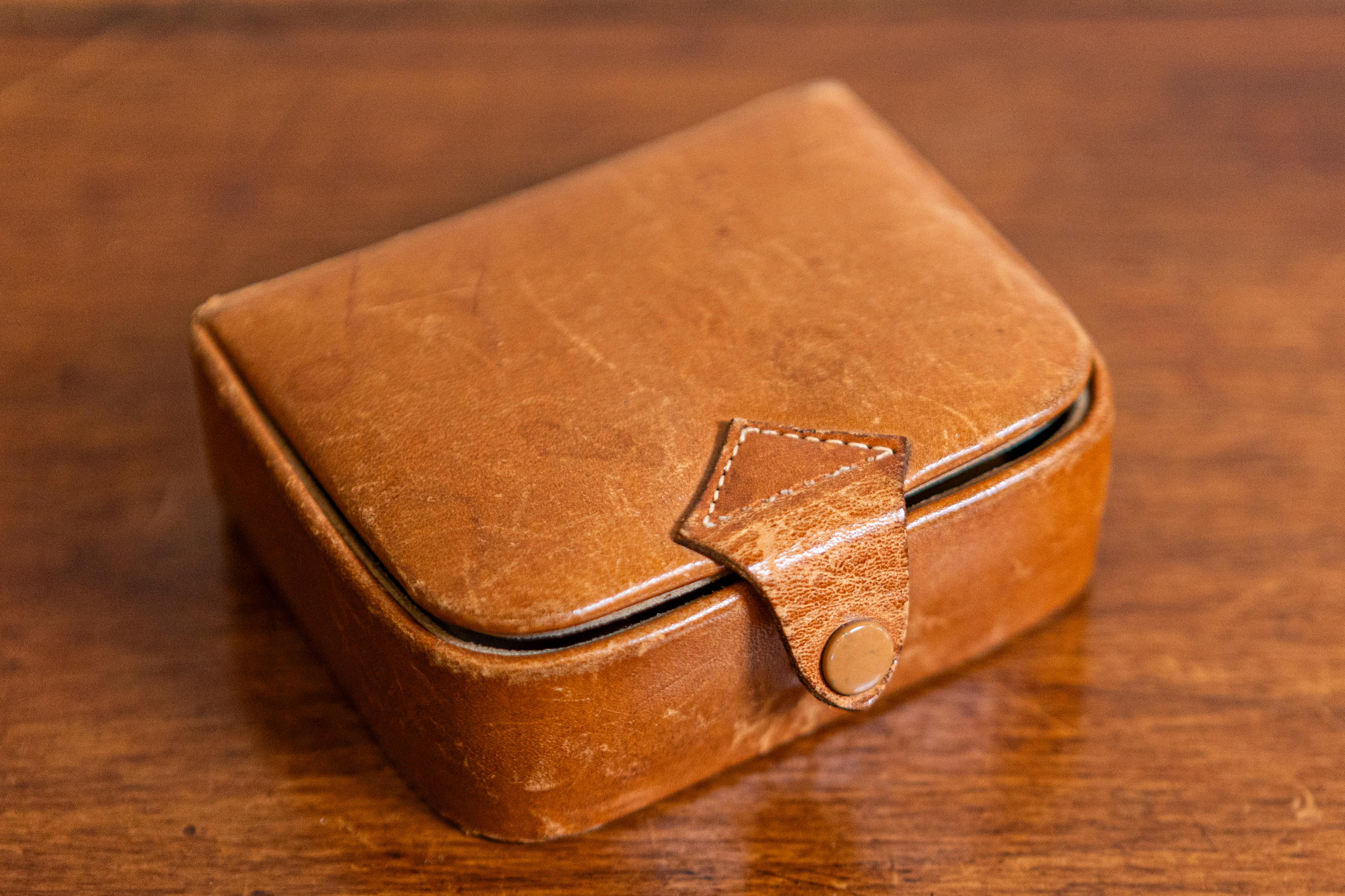 A small antique Camalier & Buckley leather case from the 20th century with buttoned strap. Founded in the 1930s in the United States, Camalier & Buckley produced this handsome leather case boasting a caramel color and a small buttoned strap. Perfect