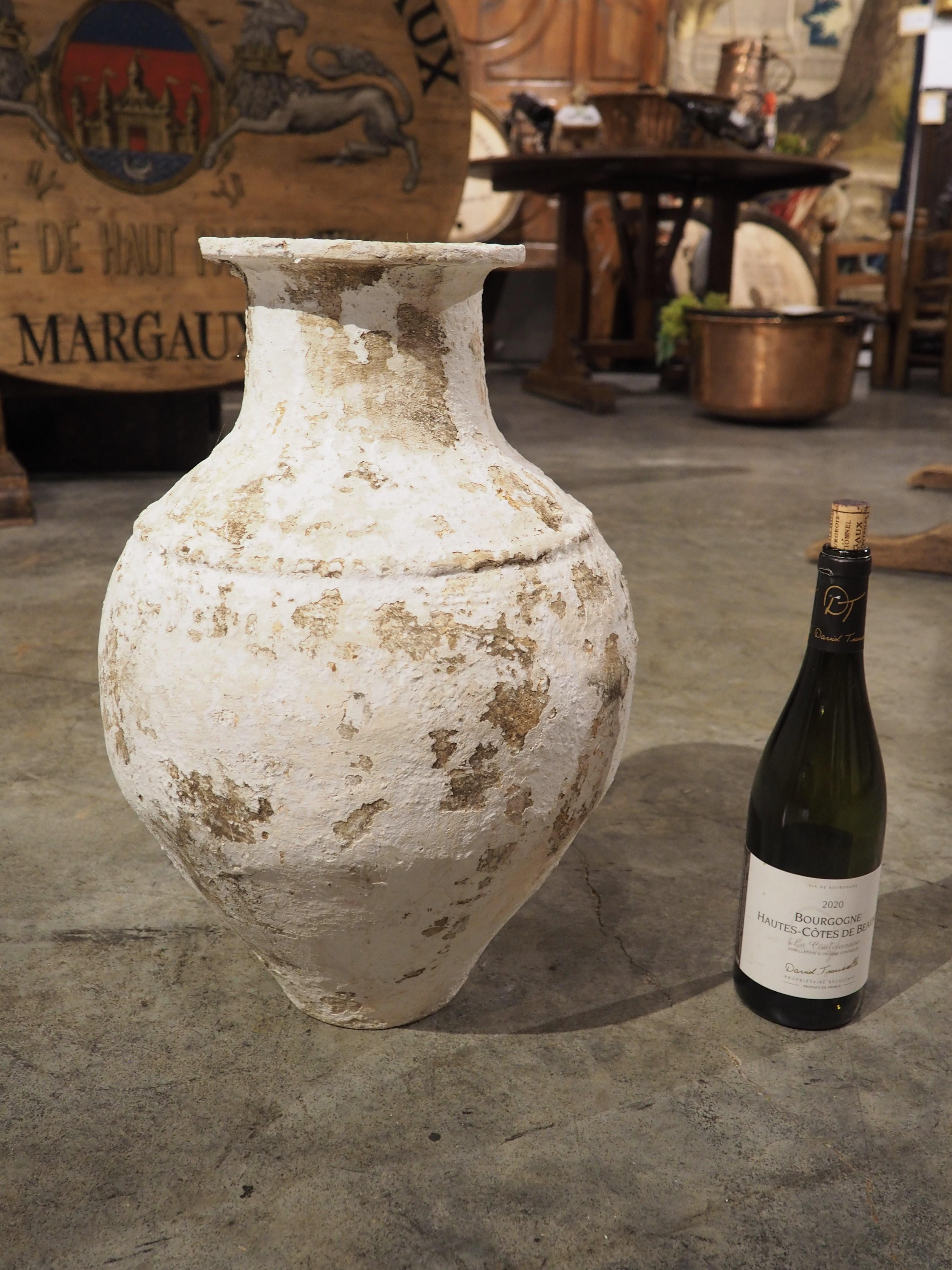 Questo vaso in terracotta, un piccolo pithos (un contenitore greco), ha proporzioni ben bilanciate, con un sottile anello sporgente appena sopra la parte più larga del corpo. L'apertura ha un bordo leggermente arrotolato, che conferisce al vaso una