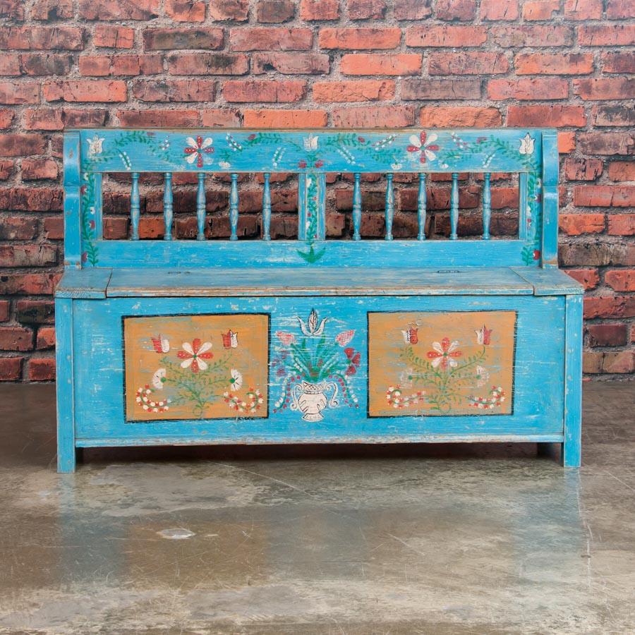 This delightful cottage style pine bench with it's spindle back and traditional folk art painted floral panels, still maintains its original sky blue paint. This 51' bench is a fun find, as many benches from this era were longer. Under the hinged