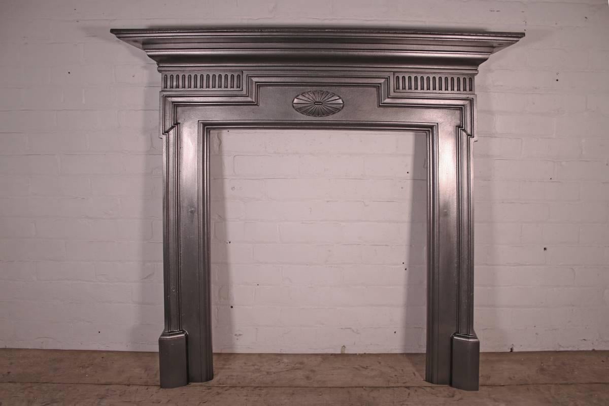 Small antique late Victorian cast iron fire surround with dog leg moulding to the jambs and a simple rosette to the frieze, circa 1895. 

Finished in traditional black grate polish giving a gun metal sheen. This finish can be changed if required.