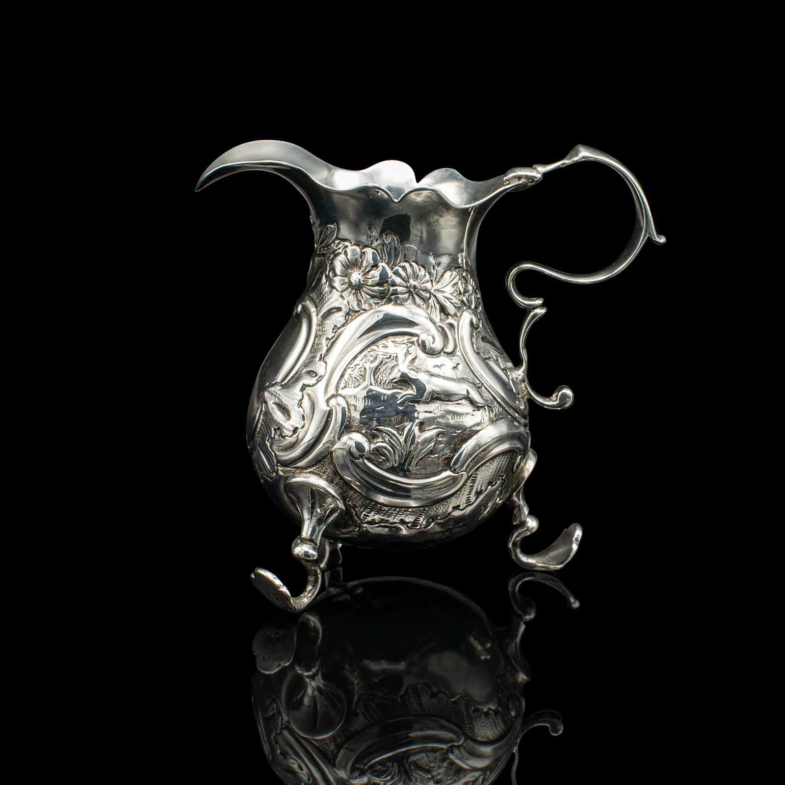 This is a small antique milk pouring jug. An English, silver breakfast table creamer, dating to the Georgian period, circa 1800.

Charmingly ornate and petite, with an appealing shine
Displays a desirable aged patina and in good original
