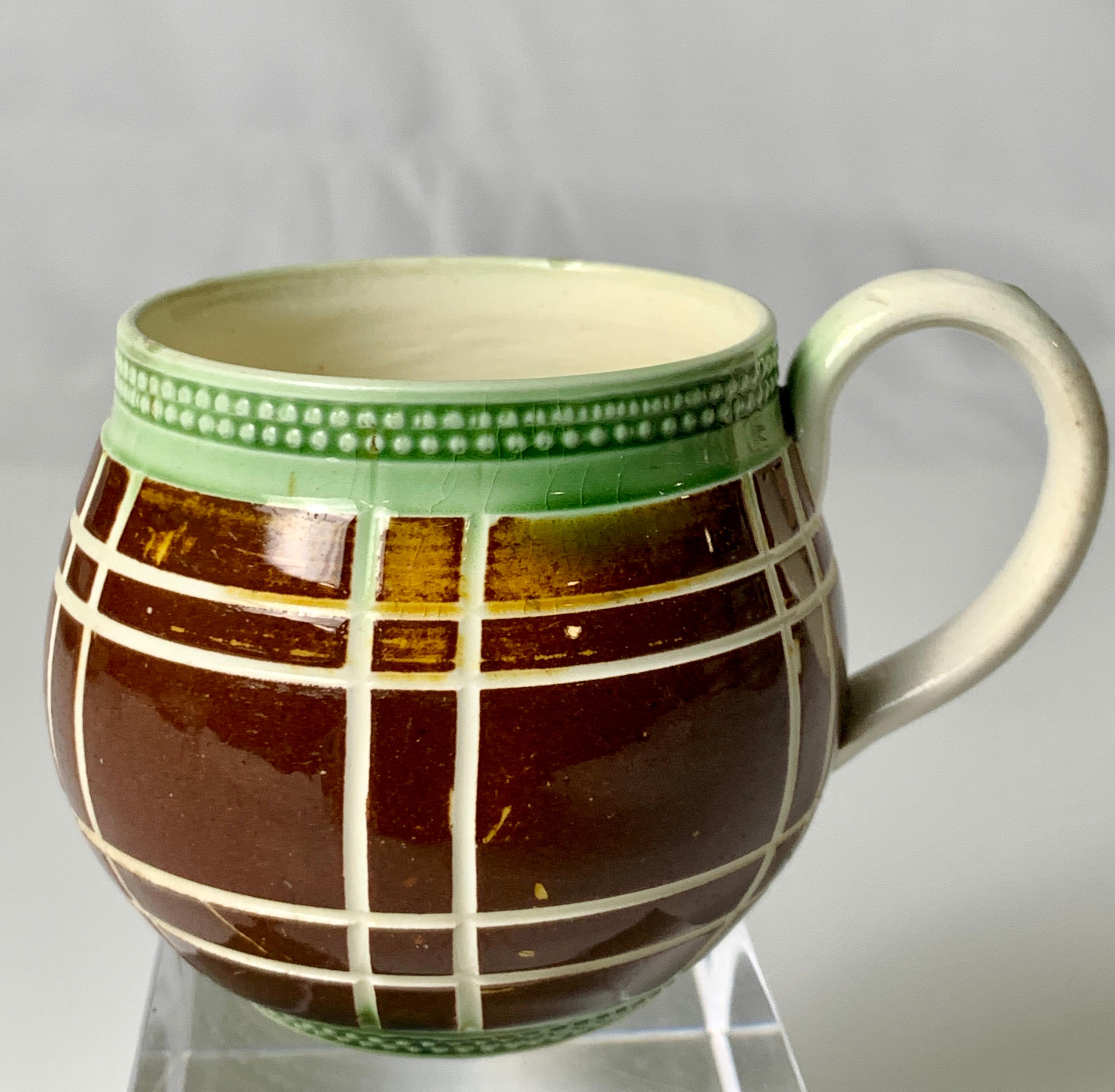 This rare Mochaware cup is a gem.
 It is a rare shape for a piece of Mochaware as it is neither a pitcher, a mug, nor a bowl. 
 The main body is decorated with brown slip and further decorated with rare vertical and horizontal engine-turned stripes