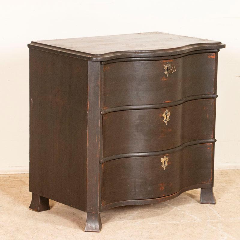 A small antique chest of drawers with brass key escutcheons and a new painted finish from Sweden. The curved front is carried down through the 3 drawer fronts. The dark brown paint almost looks black in some lighting and has been distressed in