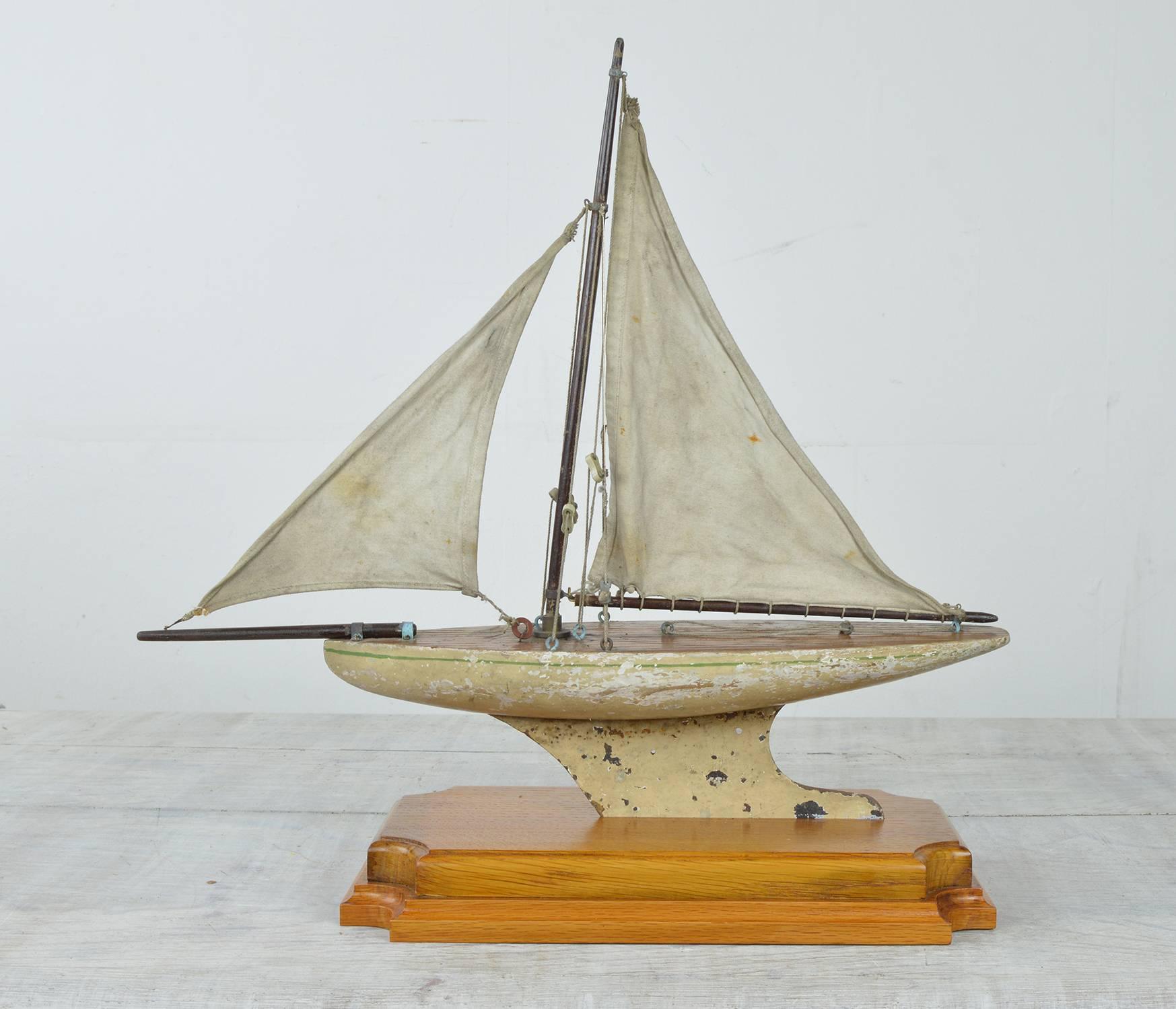 Charming little pond yacht.

Painted cream with a single green line detail.

Original paint and original canvas sails.

Slightly distressed but nothing serious. 

Mounted on a golden oak pedestal.