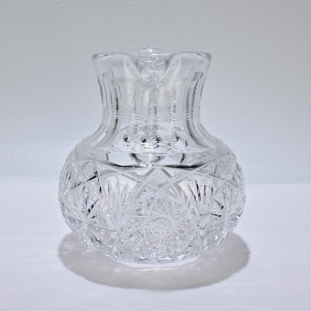 A fine antique small-scale cut glass juice or cocktail pitcher.

The body of the pitcher is bulbous or squat (like a suppressed ball) with deep cuts and a sturdy applied handle. The neck is faceted and the handle has a ribbed cut pattern.

A