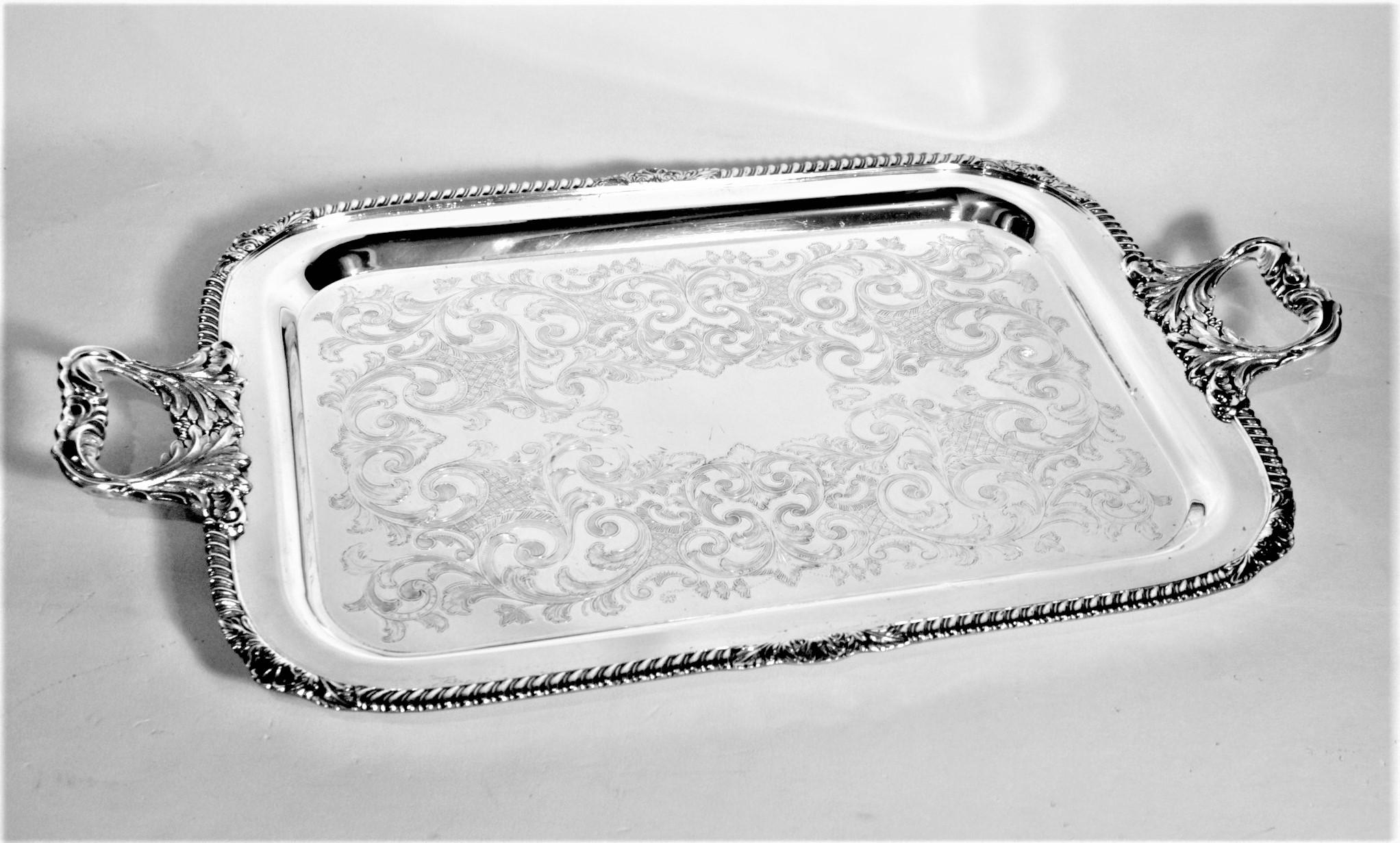 This antique styled silver plated serving tray was made by Dobman of England in approximately 1950 in a Victorian style. The tray is rectangular in shape with a rope styled beaded border and figural stylized leaves handles. The surface of the tray