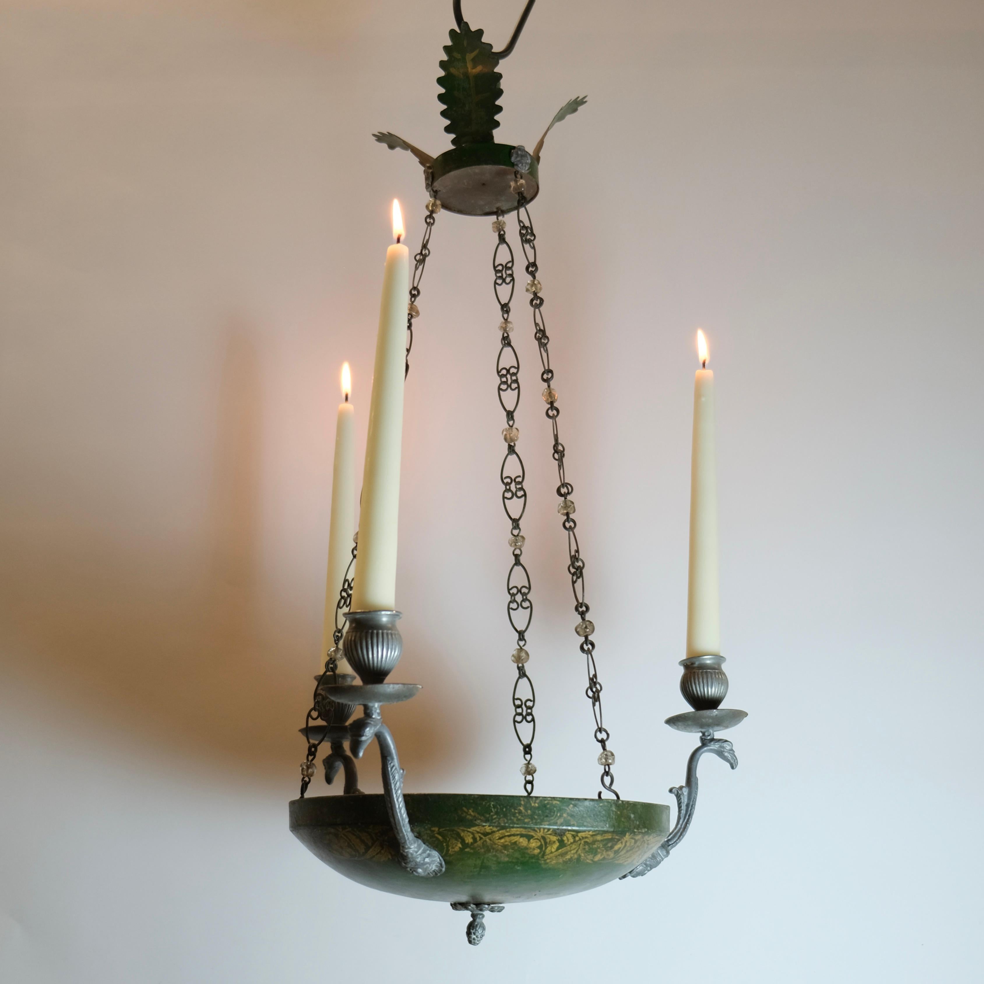 Un piccolo e affascinante lampadario svedese realizzato intorno al 1820. La ciotola a forma di piattino è stampata a mano in verde con decorazioni in oro. Le armi che raffigurano teste di uccelli e volti classici. I portacandele sono a forma di