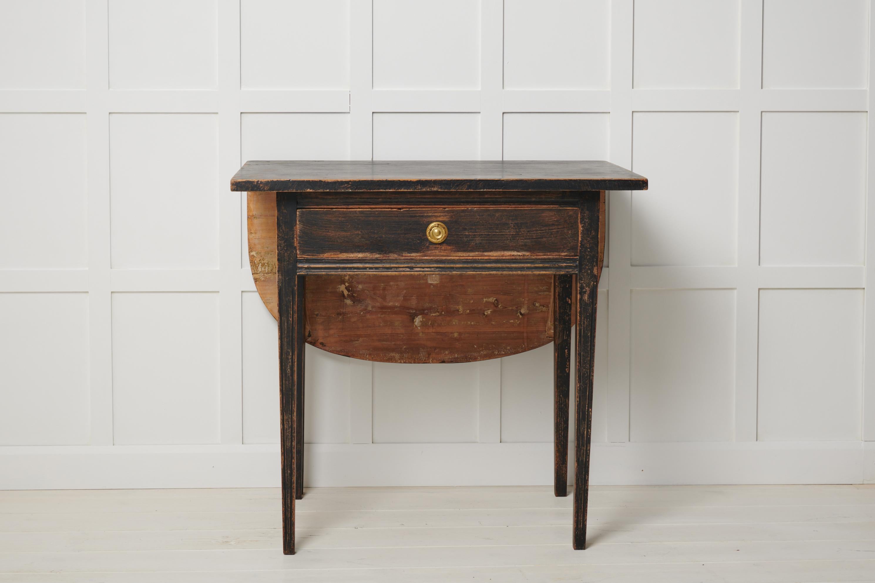Small antique black table in gustavian style from Sweden. The table is a genuine Swedish country house furniture from around 1820. The table has a rounded leaf table top on the back of the table and straight tapered legs decorated with flutes. The