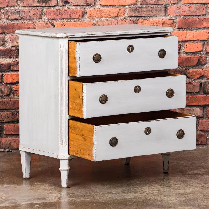 This lovely three-drawer pine chest of drawers in the Gustavian style is accentuated by fluted and mitered corners. It has recently been given an off white painted finish, adding a fresh look to the old piece. The drawers run smooth and the case is