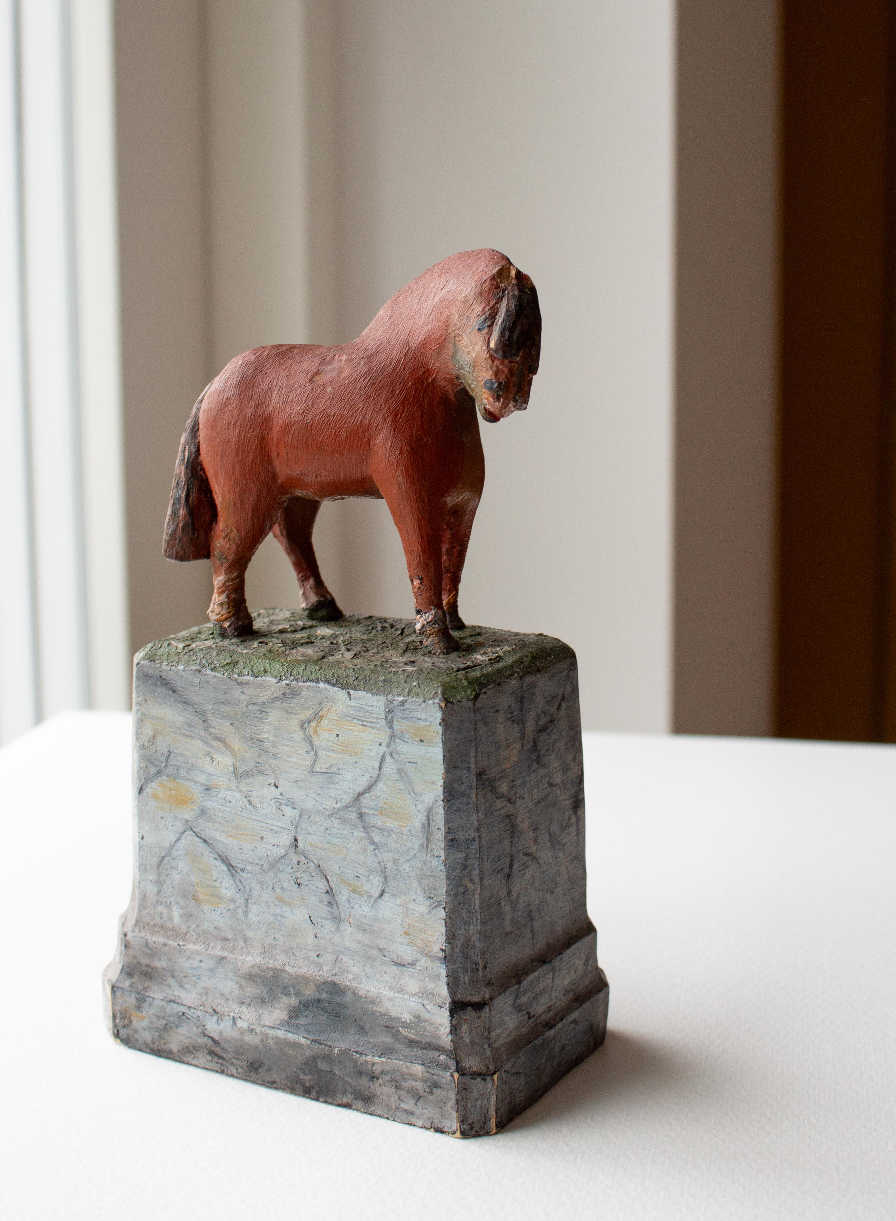 A peasant sculpture in the form of a small working, red-painted horse with a bushy mane and tail on a painted pedestal, beautifully carved and painted wood. 
On the underside, a text in pencil: Memory of Harald (probably the horse's name)