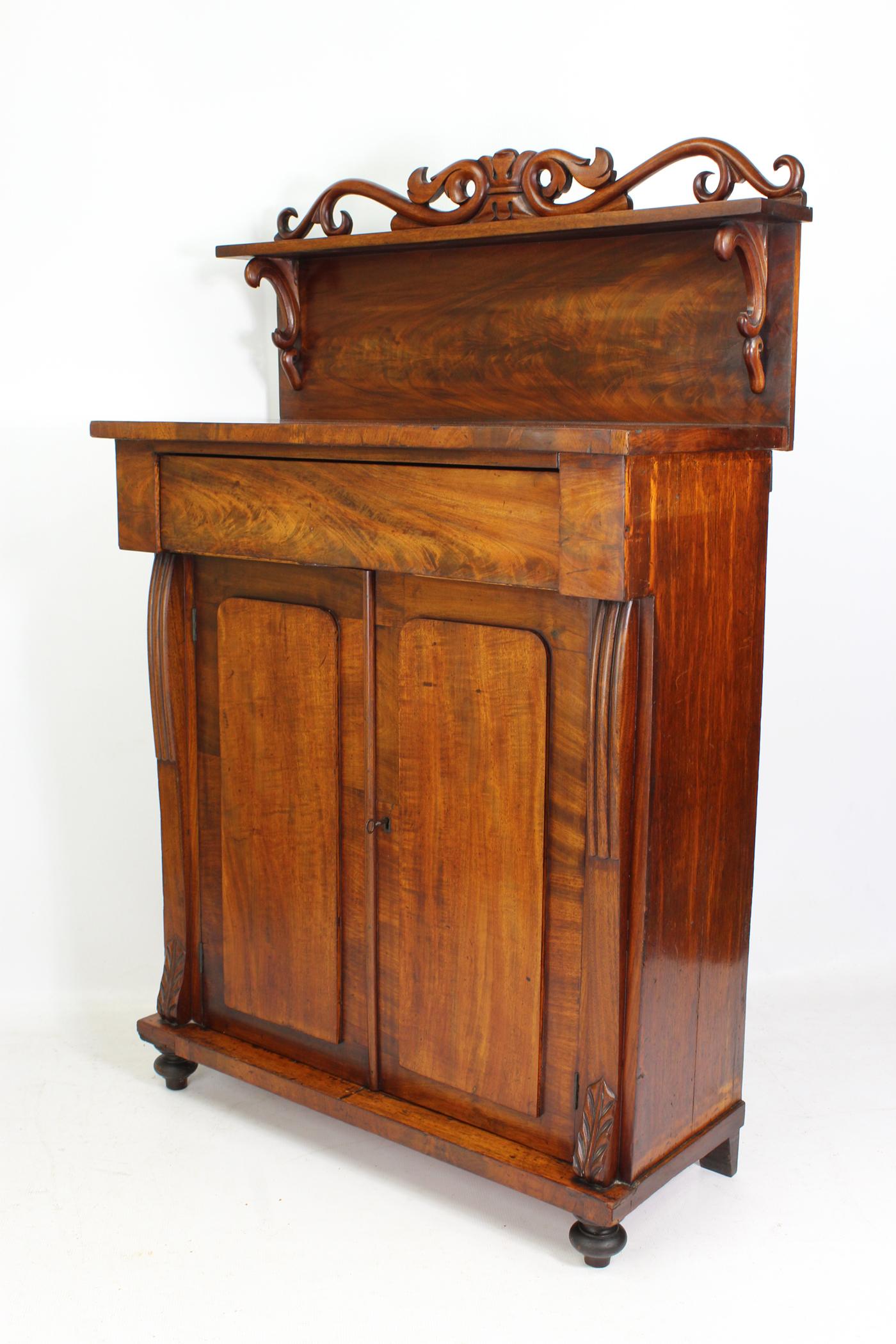 A good quality small antique Victorian chiffonier sideboard in beautifully figured mahogany dating from circa 1850. Having single frieze drawer above two cupboard doors enclosing a fixed single shelf, with gallery top with carved pelmet and shaped