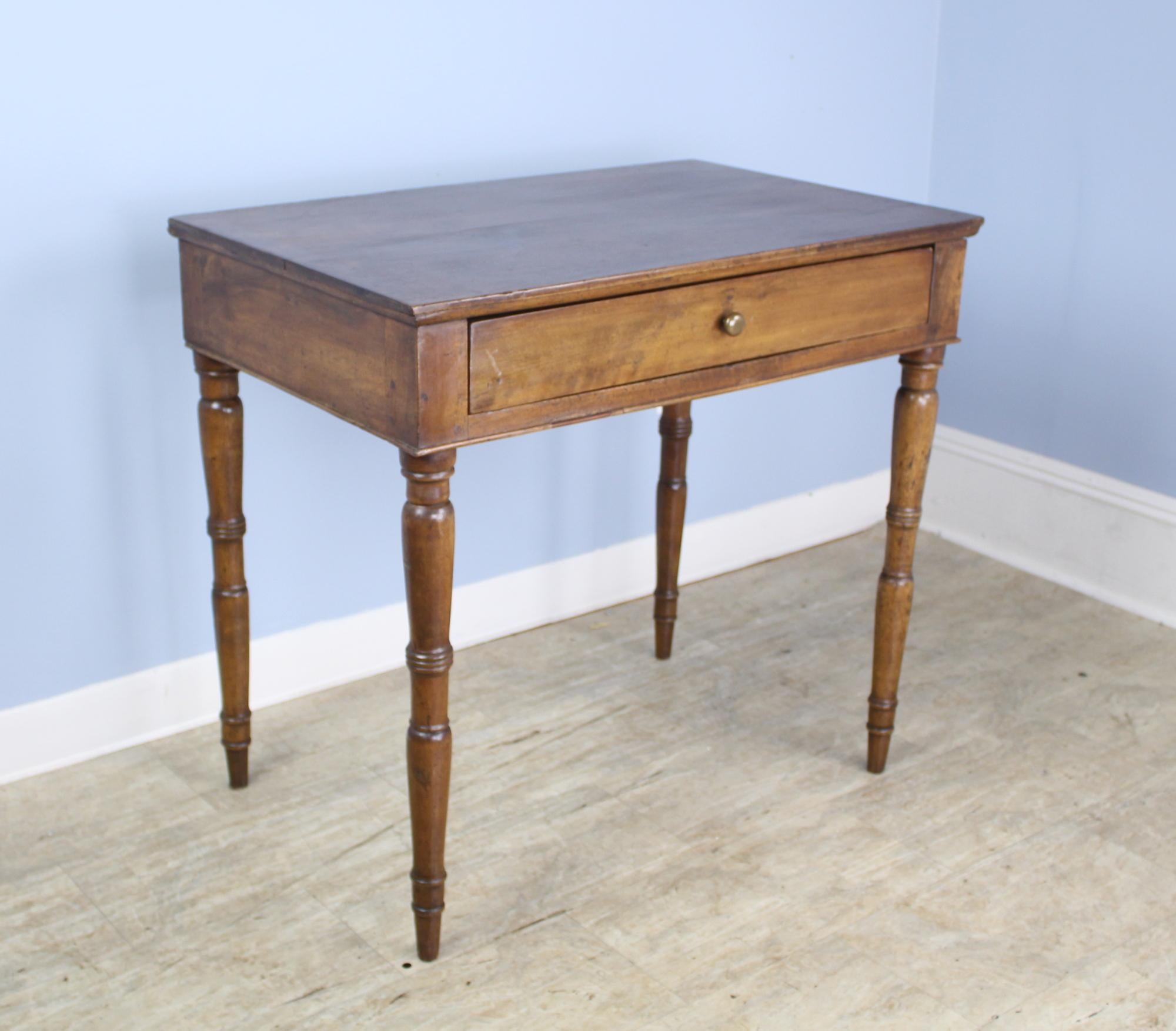 A small writing table in beautifully grained walnut with a book match top. The turned legs add an exciting design element and are glossy and well-shaped. The single roomy drawer is deep and closes snugly. 25 inch apron is good for knees. Small