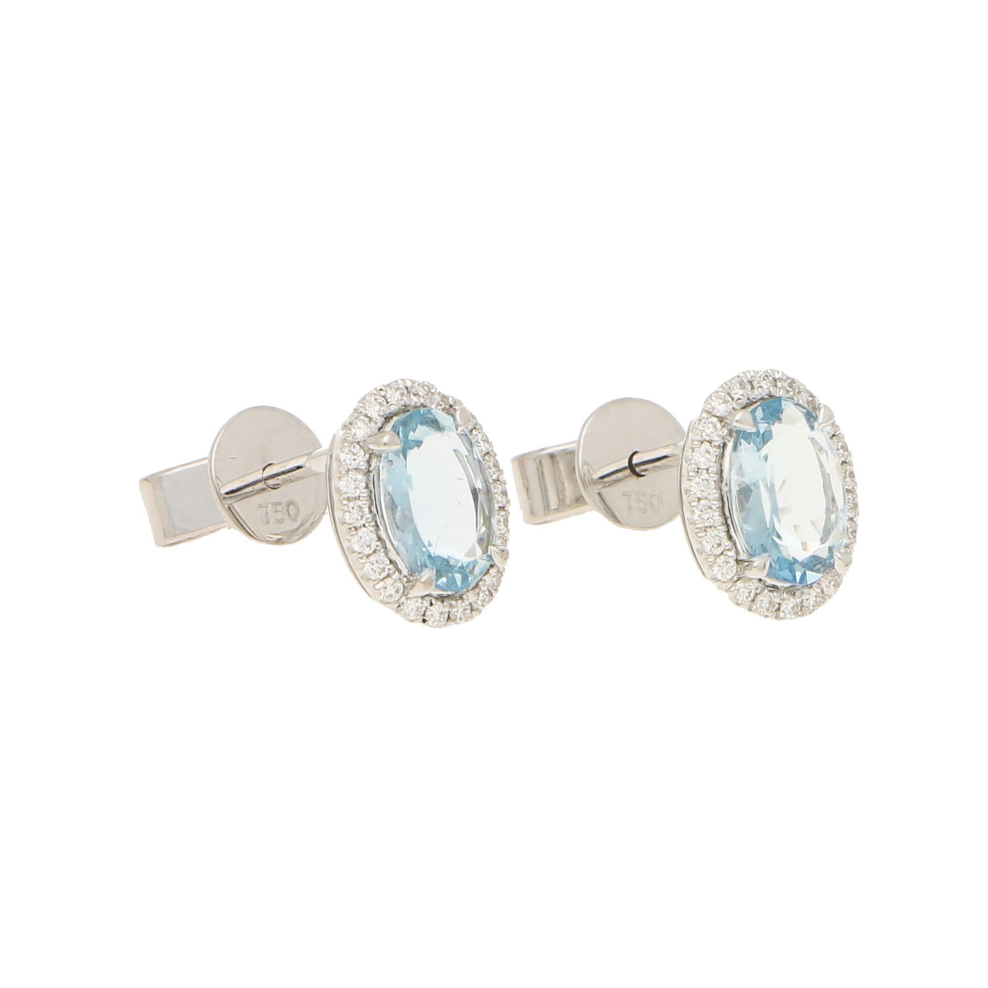 A lovely pair of aquamarine and diamond oval halo earrings set in 18k white gold.

Each earring centrally features a beautiful blue coloured oval shaped aquamarine surrounded by a halo of 22 round brilliant-cut diamonds. All of the stones are set to