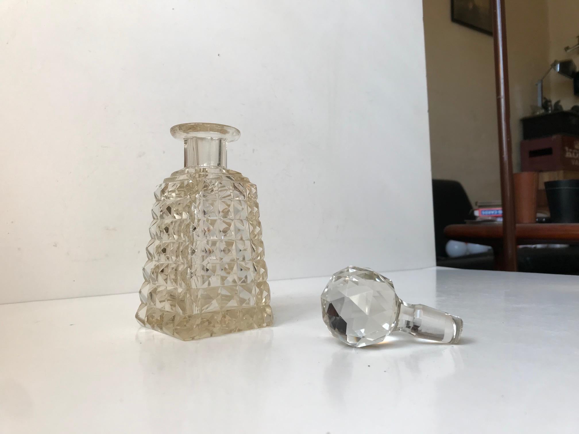 Small ornate crystal decanter cut with diamond patterns and set with a faceted spherical stopper. Probably made by Holmegaard in Denmark during the 1920s who alongside a few Czech makers used the edged star as marking beneath the base. It has a