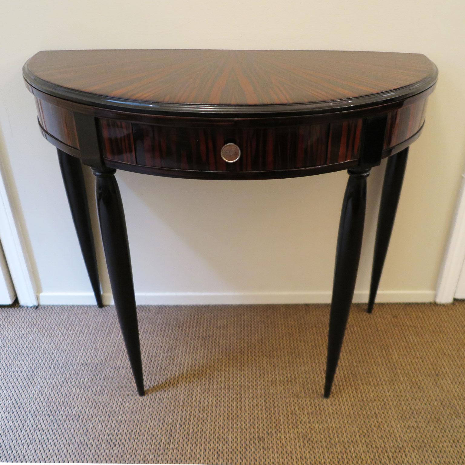 Small demilune console with Macassar ebony with a starburst pattern on top. Black lacquer rounded, tapered legs and details. Small curved centre drawer with silver knob.