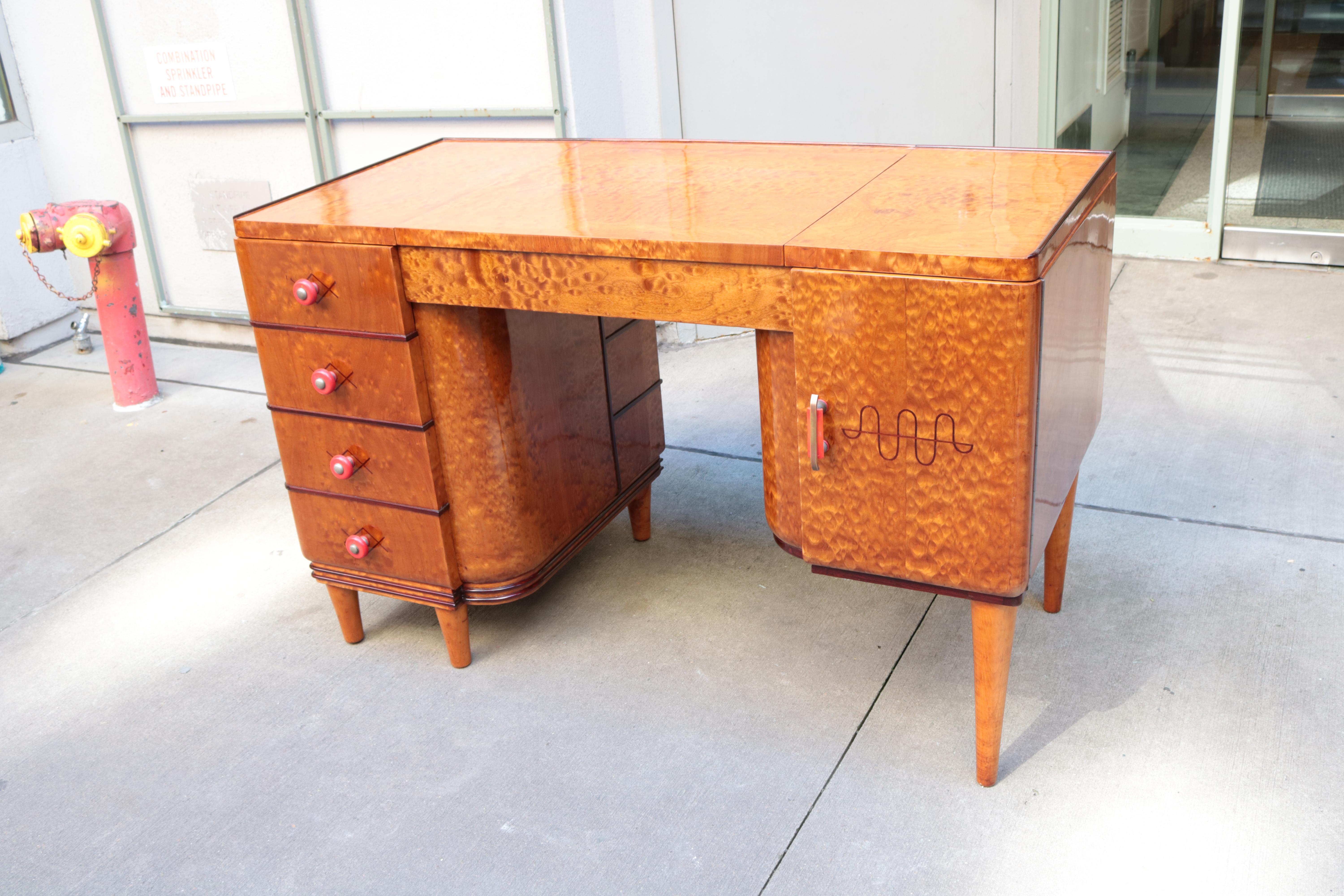 An Art Deco small desk. Amboyna with inlaid details, 
red bakelite and brass pulls. Desk features four drawers 
a storage cabinet and an additional storage area underneath a lift up top.