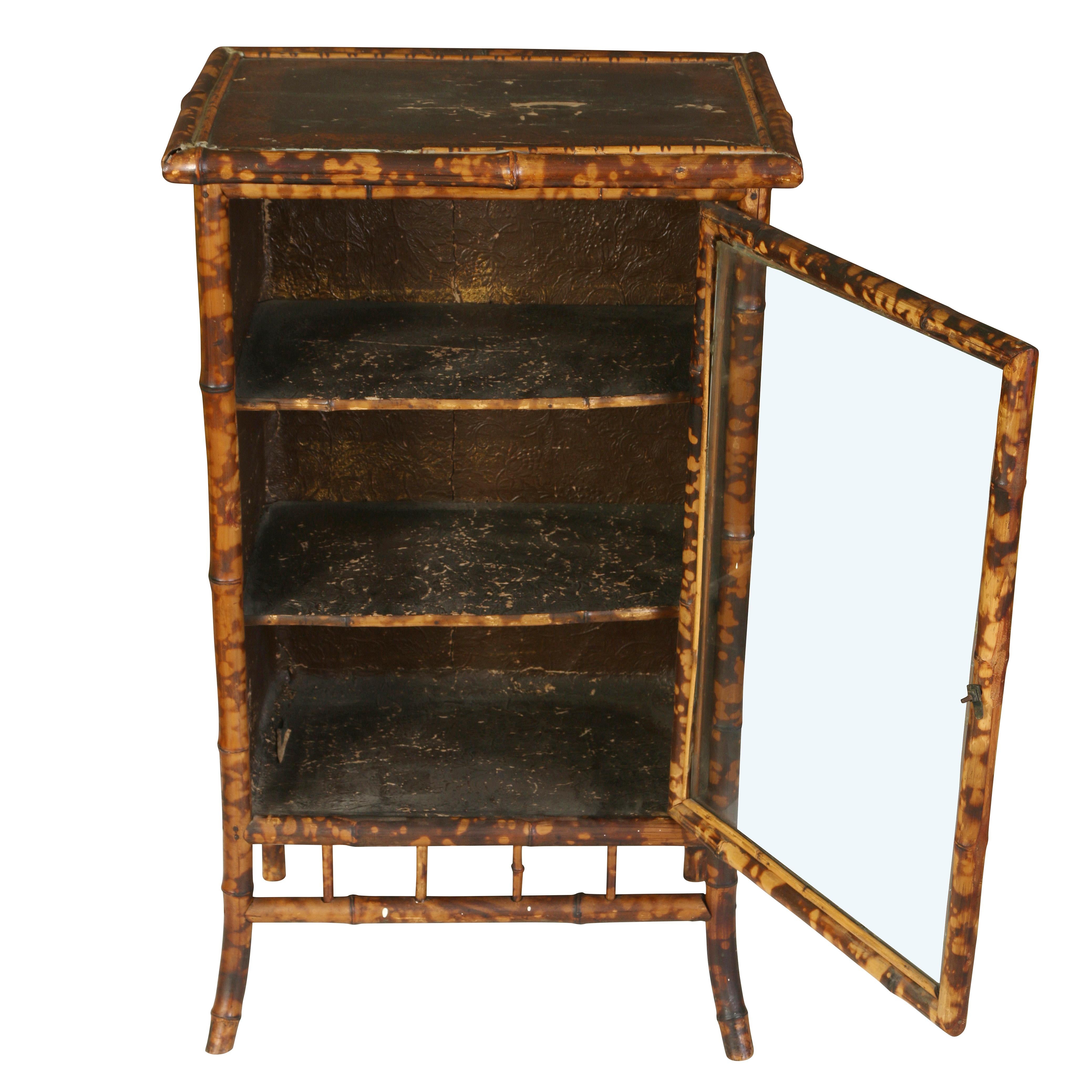 A handsome little bamboo cabinet in a faux tortoiseshell finish, with three shelves and a glass door.  The painted finish on the top and sides has developed a lovely time-worn patina, giving it great character and personality.  