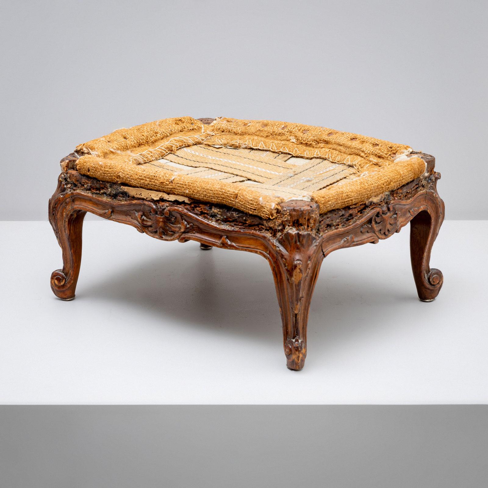 Petit pouf avec un cadre en bois sculpté, des pieds rococo et une décoration en forme de vrille. Le tabouret n'a pas été restauré.