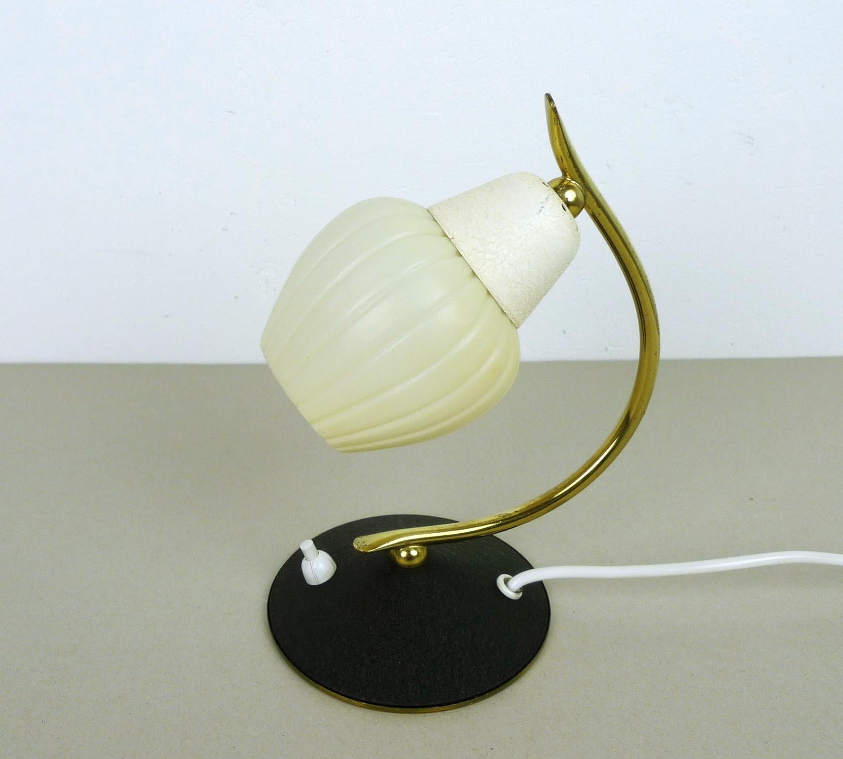Small bedside lamp from the 1950s with a white plastic shade on a brass handle on a round, black-lacquered stand. The bedside lamp has a pressure switch on the Stand and is operated with an E 14 lamp socket. The lamp is in good vintage condition.