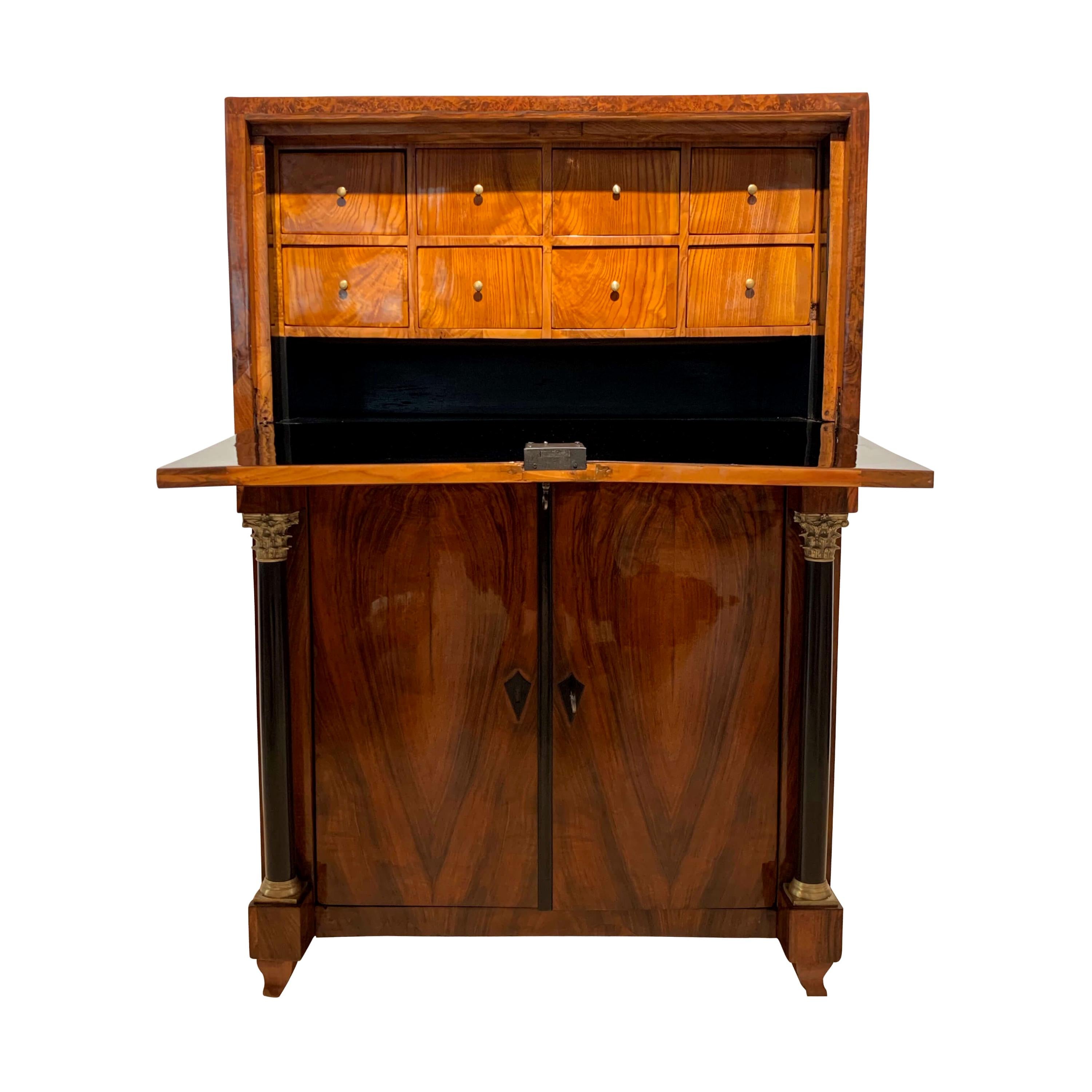 Extraordinary small Biedermeier Secretaire / writing desk from Austria, Vienna, 1820s.

Wonderful book-matched walnut veneer on the outside and walnut roots veneer at the cornice rims.
Inside with eight long drawers, veneered in Ash with brass