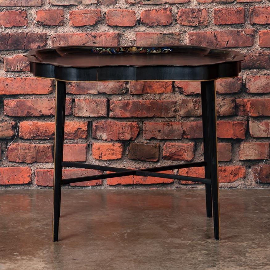 Cette table anglaise unique, avec son plateau amovible en métal peint en noir, a beaucoup de caractère dans un petit espace. Remarquez l'incrustation de nacre qui est insérée sur le plat du plateau à chacun des quatre points peints Folk Art. Les