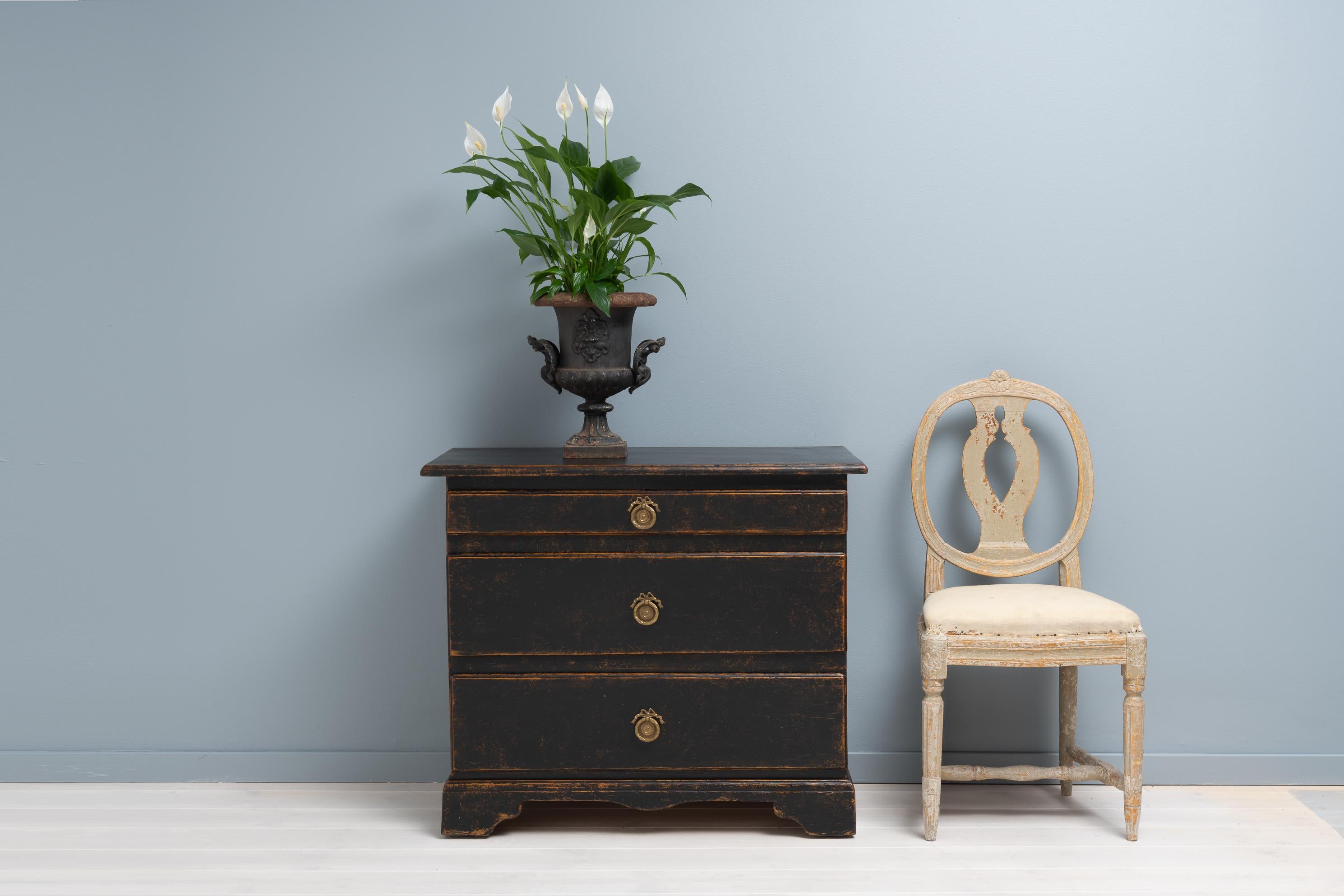 Small black Swedish baroque chest of drawers from the late 1700s. The chest is painted pine with patina and distress that emphasises the shapes and contours of the chest. It has three drawers with the top one being smaller. The chest is on the