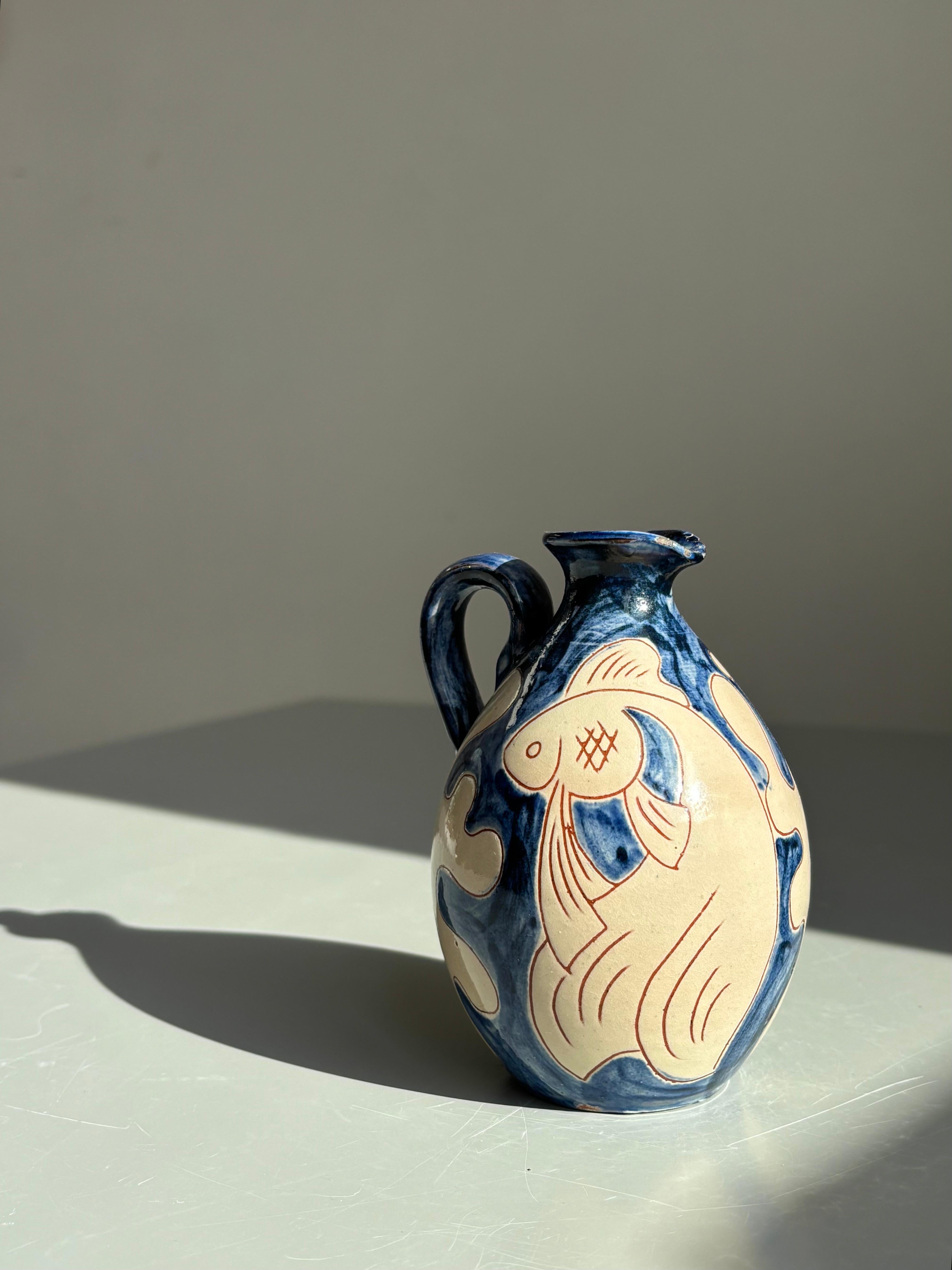 Vaso per bottiglie in ceramica decorato con una scena subacquea con pesci e forme organiche e bolle. Smalto crema e blu scuro. Maniglia e beccuccio piccoli. Firmato sotto la base.
Danimarca, anni '60.