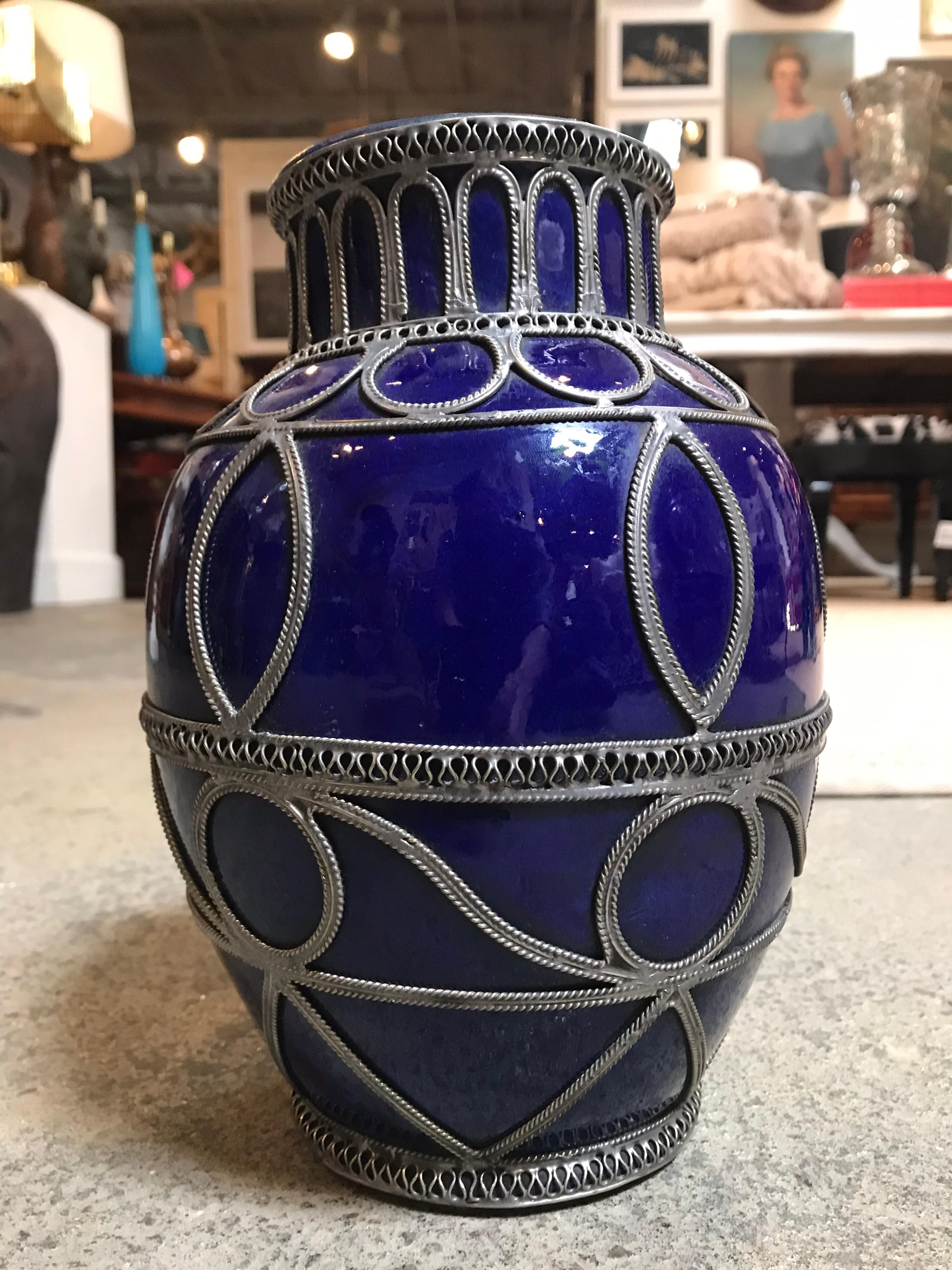 This small, dark blue Moroccan pot is hand painted and has a ceramic glaze. It is decorated with various ribbons of silver-like metal providing round geometric patterns throughout.