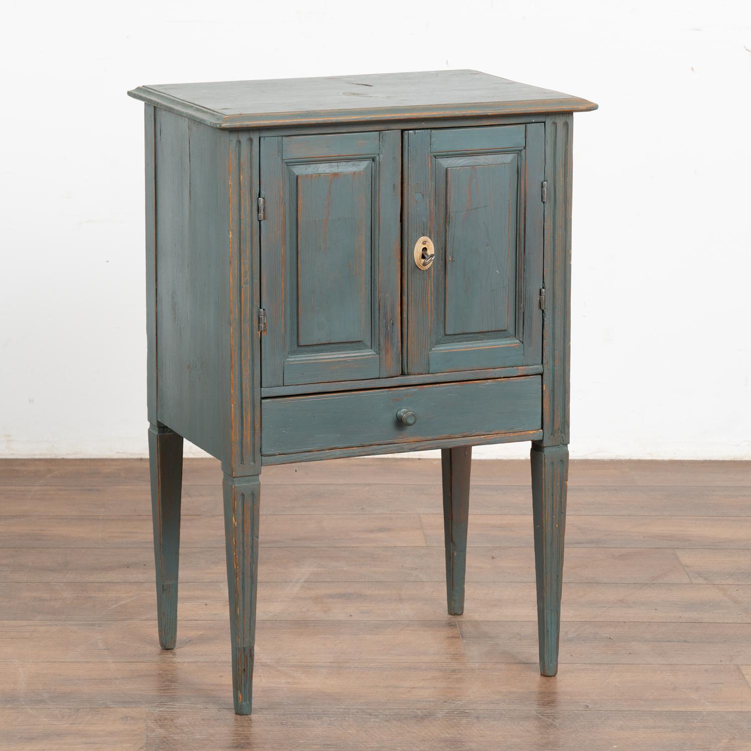 Small Swedish country pine cabinet standing on fluted tapered legs; may serve also as a nightstand or side table.
Two cabinet doors rest over a single drawer.
The old lock still functions on the right cabinet door and key is used to open.
The newer