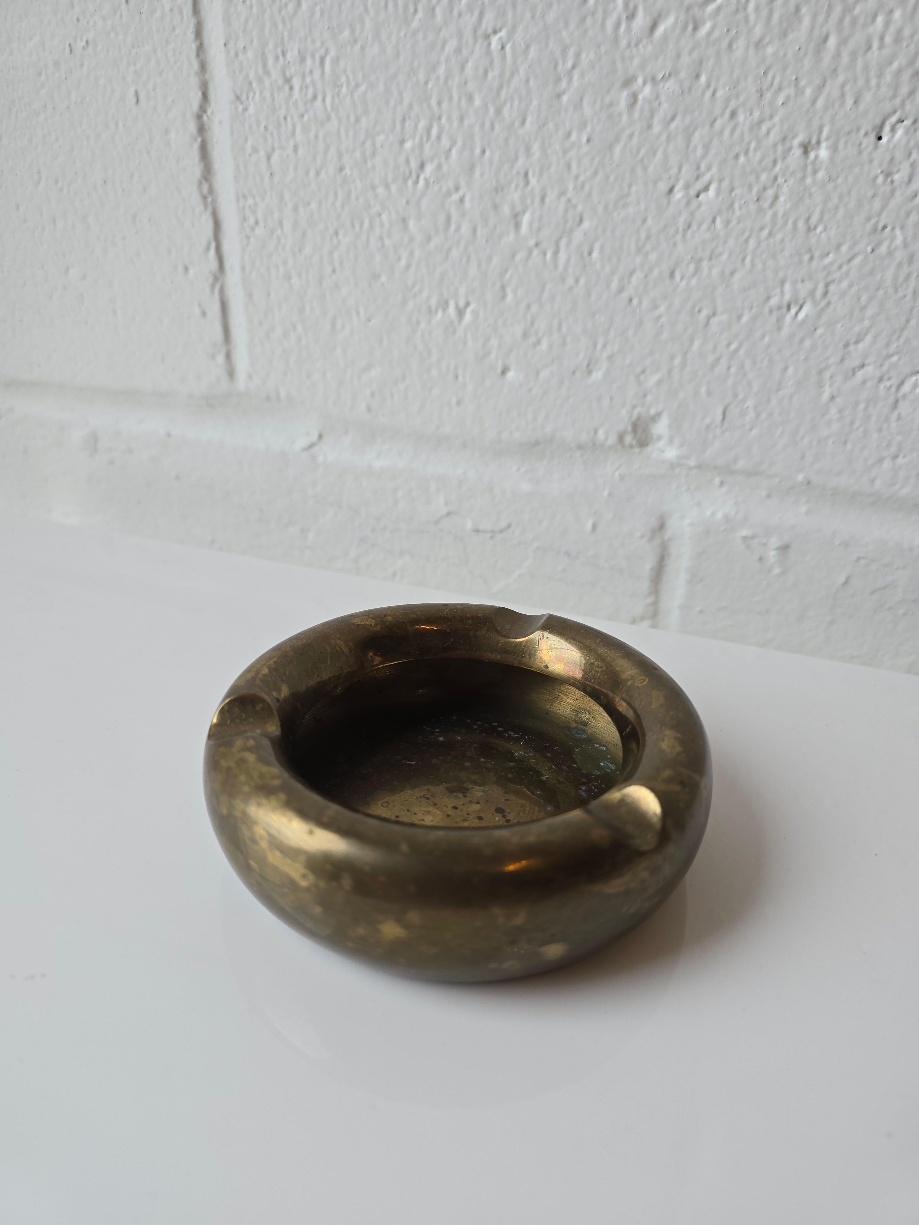 Round brass ashtray with three cigarette rest holders. It was made circa 1960s. It has patina and wear which adds to the character of the ashtray.
In overall good/fair condition with patina, wear throughout. 