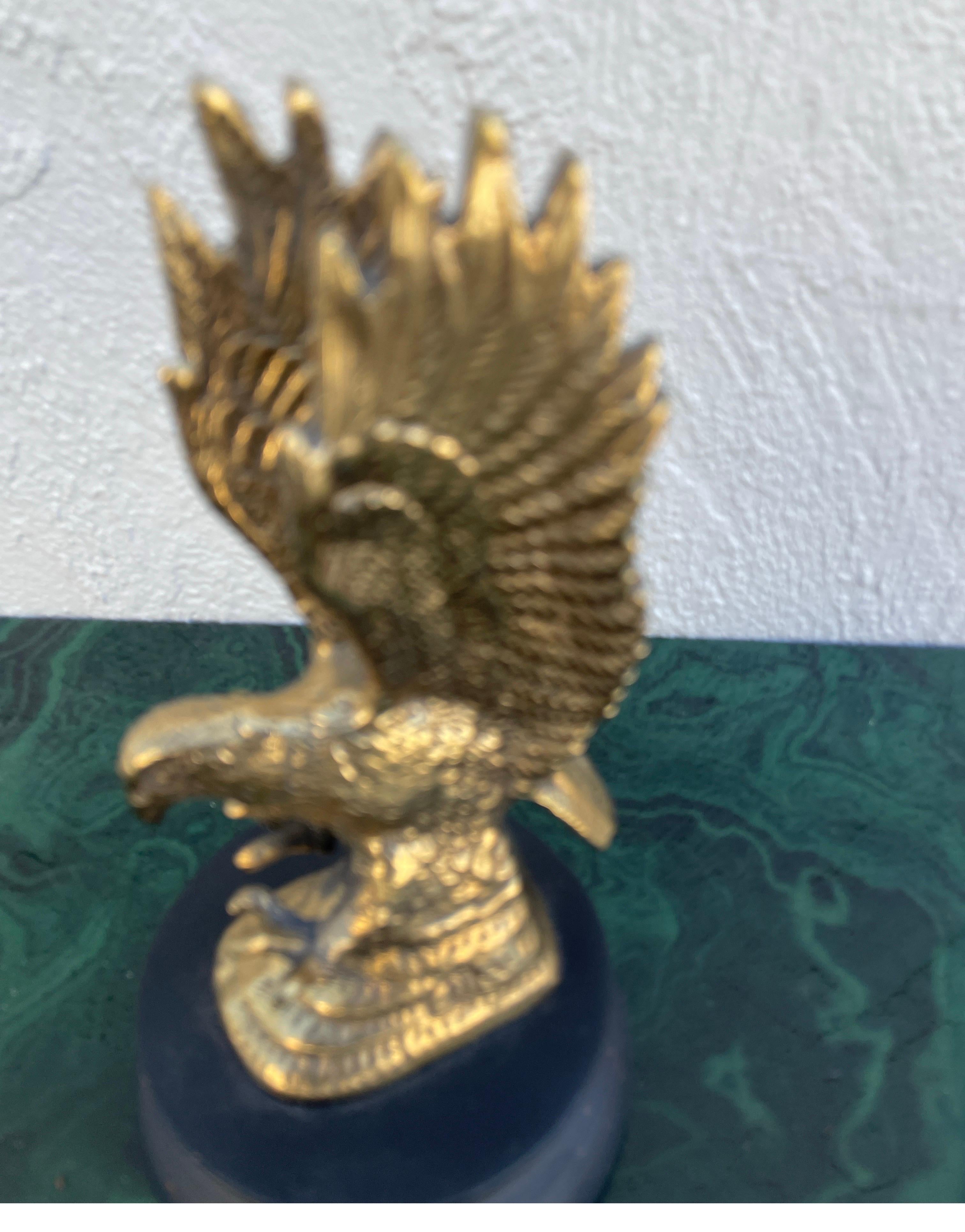 Aquila in ottone massiccio con ali spiegate montata su un basamento in legno dipinto di nero.