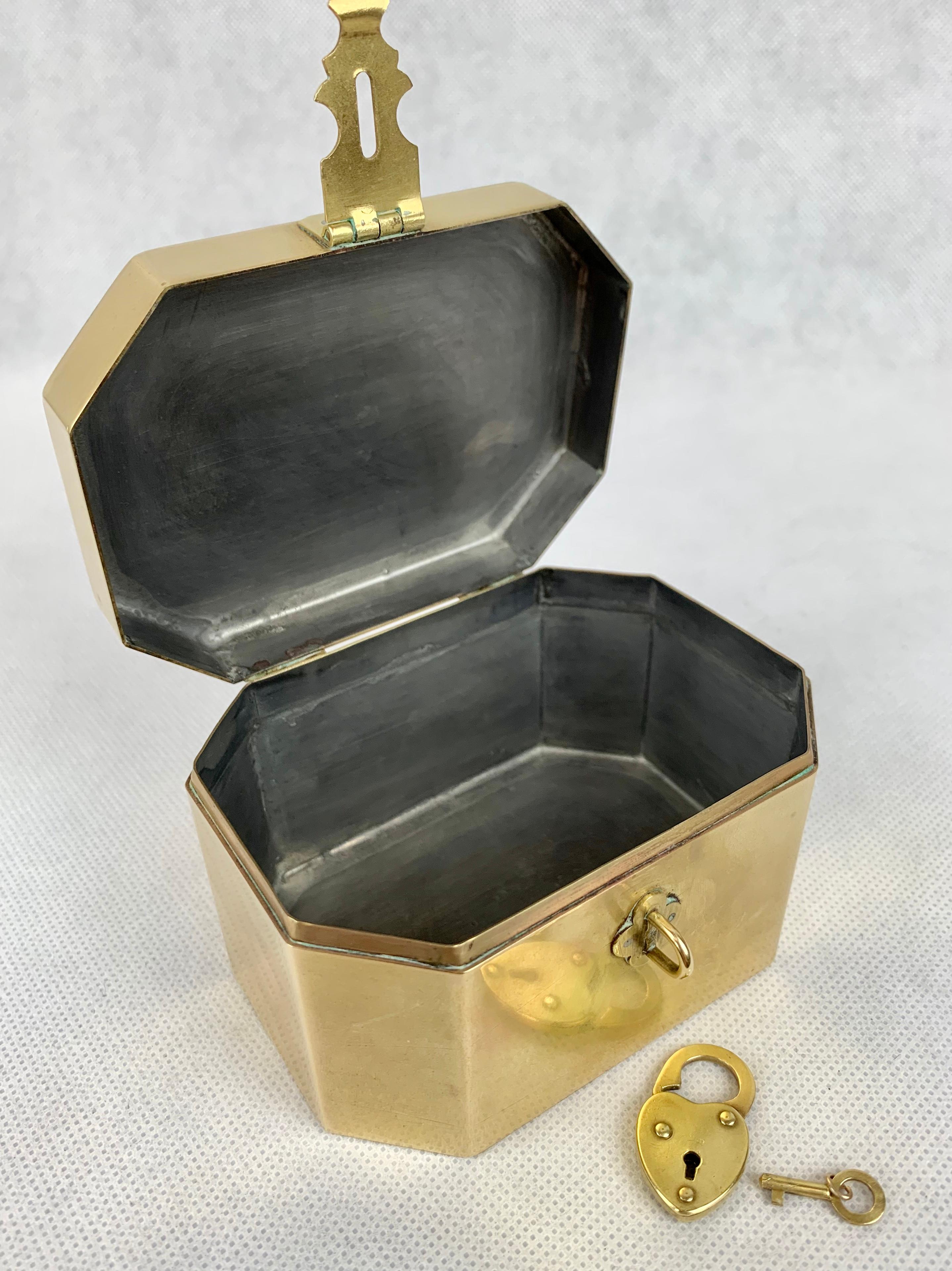 Small brass tea caddy with original heart shaped lock and tiny key. The rectangular shape has cut corners and a pewter lining. It is very special to find keys and locks married to the item. Tea was expensive and as a result kept under lock and key.
