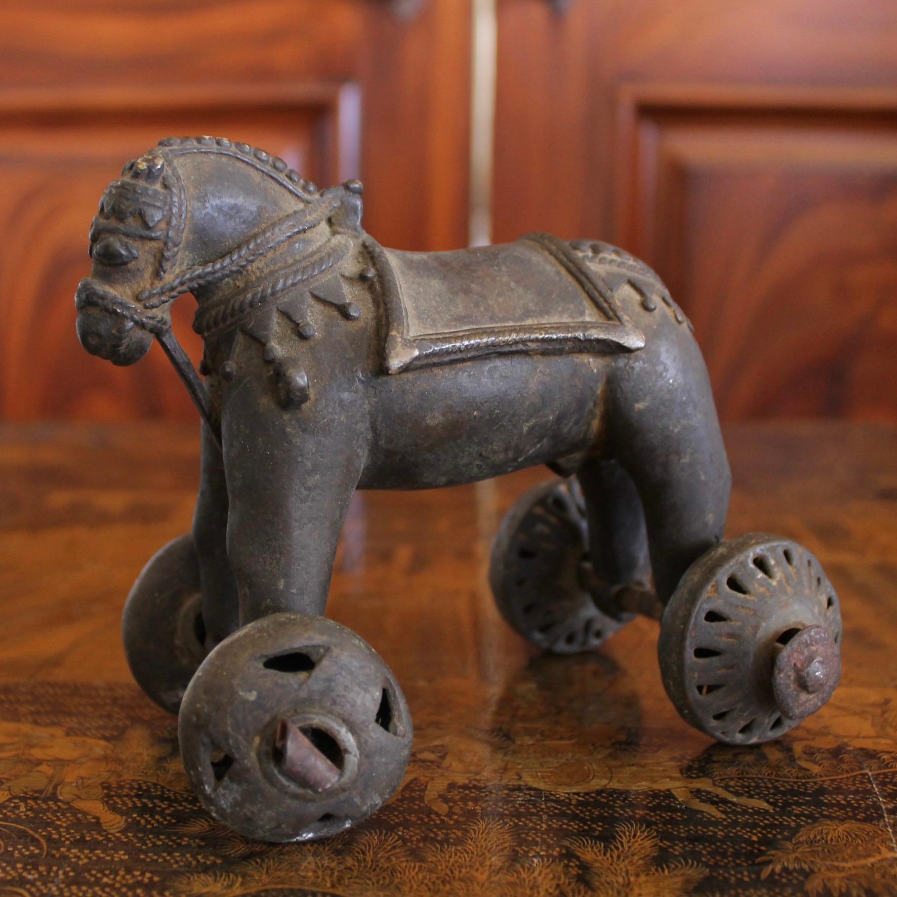 A charming cast bronze horse with elaborate caparisoned harness and braided mane, the legs ending in wheeled axels. This was a temple offering, of a type known as “temple toys,” left by the devout at Hindu temples. Thick metal axels and wheels. This