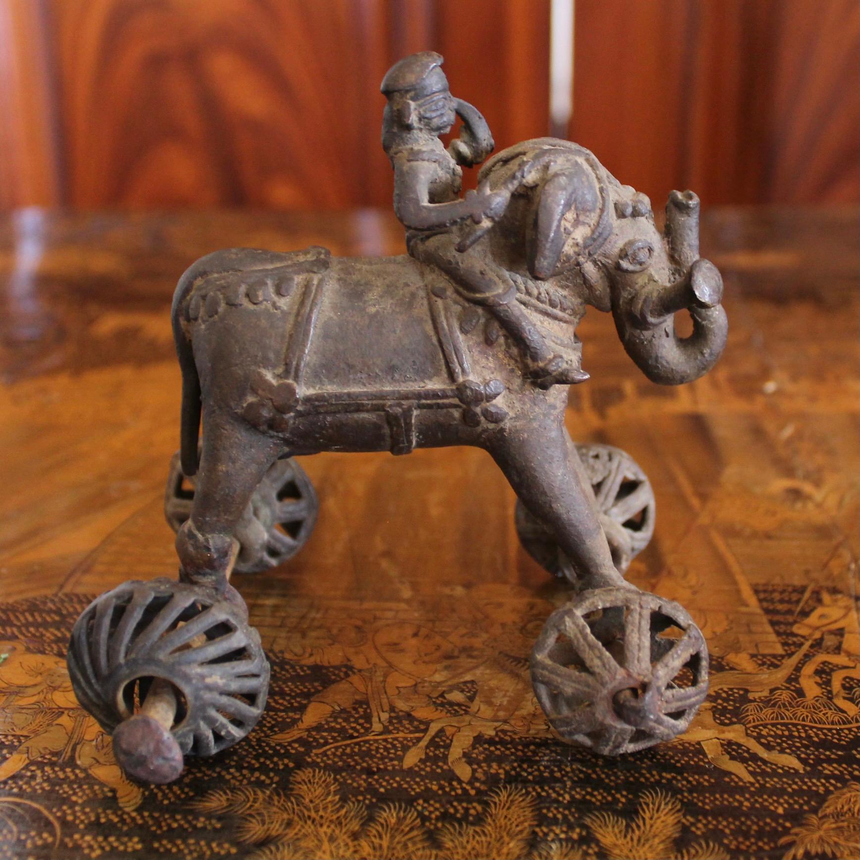 The caparisoned elephant stands with trunk raised, while the little rider figure perches high on its neck holding a scythe. Thick metal axels and wheels. Charming irregularities and rustic execution. This was a temple offering, of a type known as