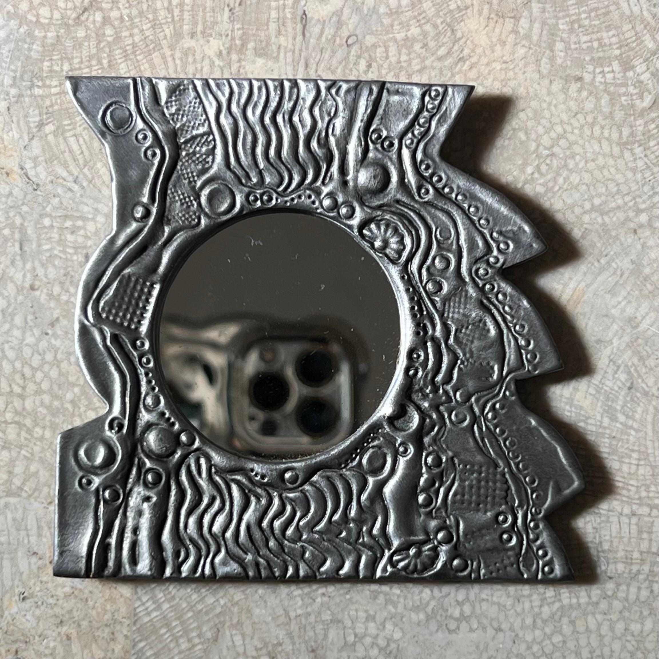 Ein brutalistischer Miniatur-Aluminium-Wandspiegel des Metallkünstlers Donald Drumm, signiert auf der Rückseite, Ende des zwanzigsten Jahrhunderts. Handgefertigt mit Drumm's charakteristischen illustrativen Motiven mit einer starken skurrilen und