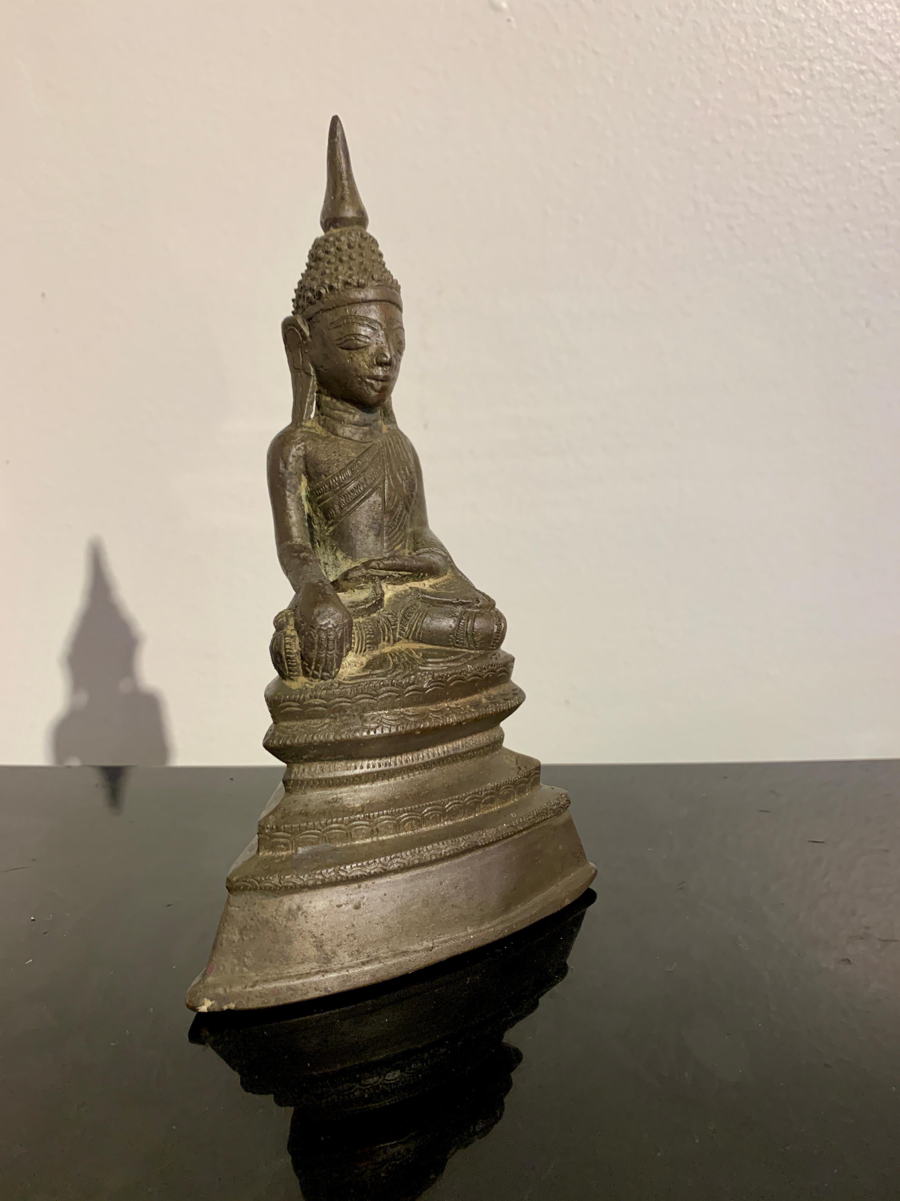 A decidedly charming small cast bronze figure of the Buddha, 18th century, Shan Tai Yai peoples, Burma (Myanmar). 

The small image of the Buddha is portrayed seated in full lotus position, both soles of the feet pointed upwards. His hands perform