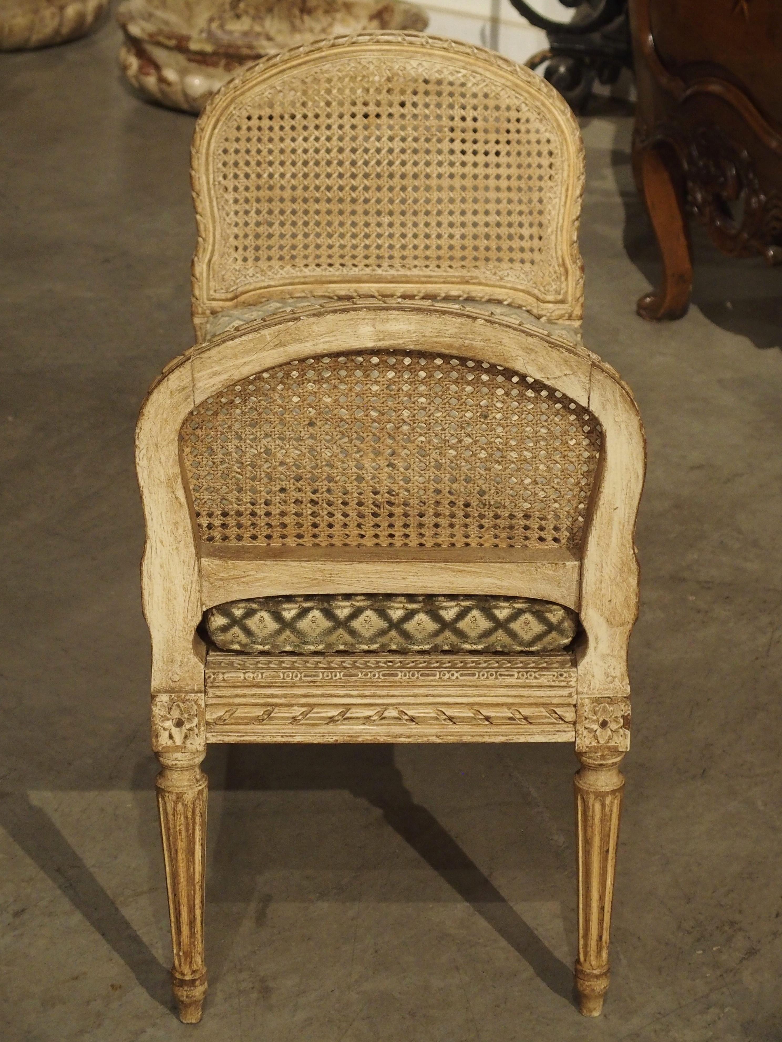This small caned and painted banquette is from France, circa 1890. Banquettes originated in the 15th century and were designed to be light enough to be transported easily.

A plush cream-colored velvet cushion with green latticework covers the
