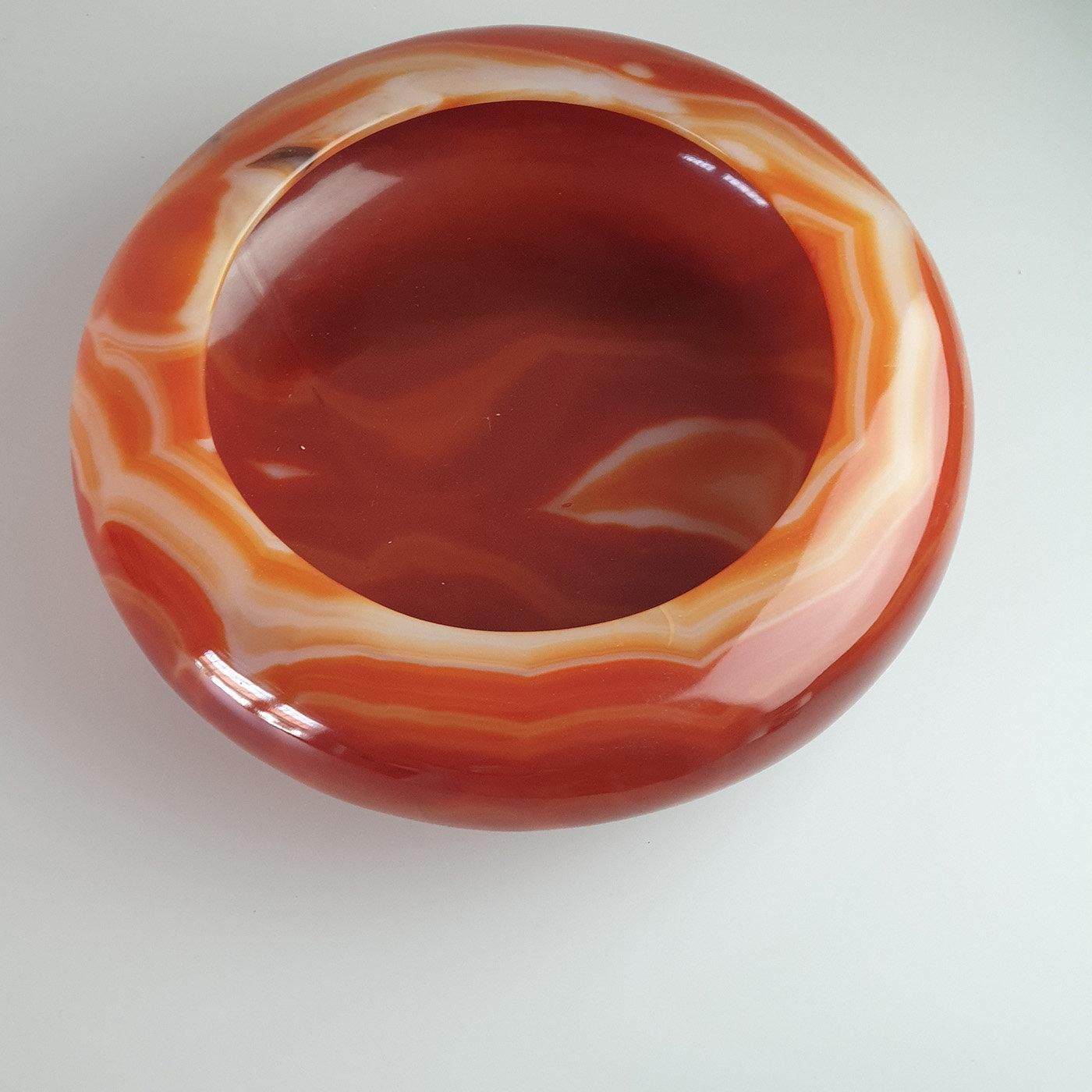 Accurately manufactured from a single piece of brilliant carnelian agate, this vide-poche bowl is a one-of-a-kind piece of decor. Adorned with delicately rounded edges, it features a range of colors, from a dark red to a rusty brown and pale-pink.