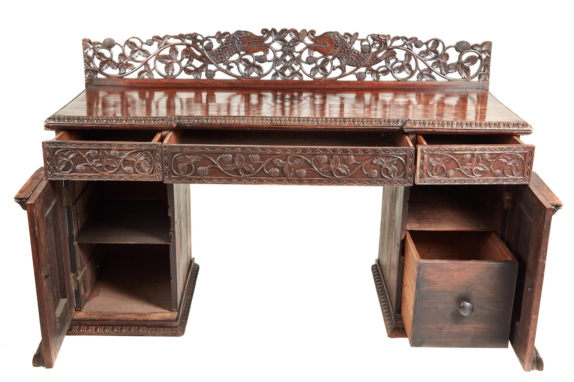 This is a small carved Anglo-Indian padouk inverted breakfront pedestal sideboard. It has a finely carved back with acorn and oak leaves surrounding a lovely pair of carp. The inverted breakfront top with a gadrooned edge, three carved drawers to