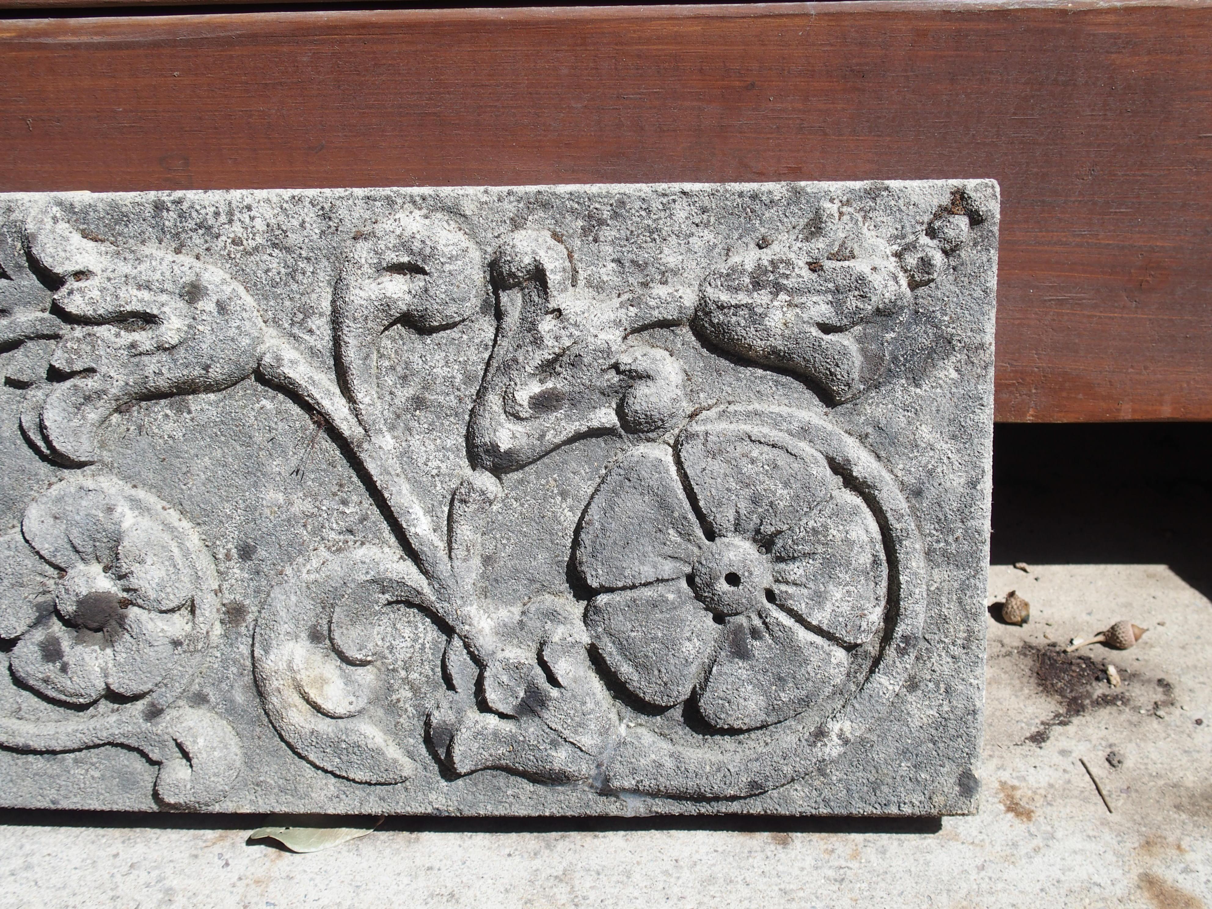 From Italy, this small limestone plaque depicts a hand-carved foliate rinceau dotted with two large flowers in bas relief. Presented horizontally, the tendrils of the plant meanders the entire length of the rectangular plaque. The gray limestone has