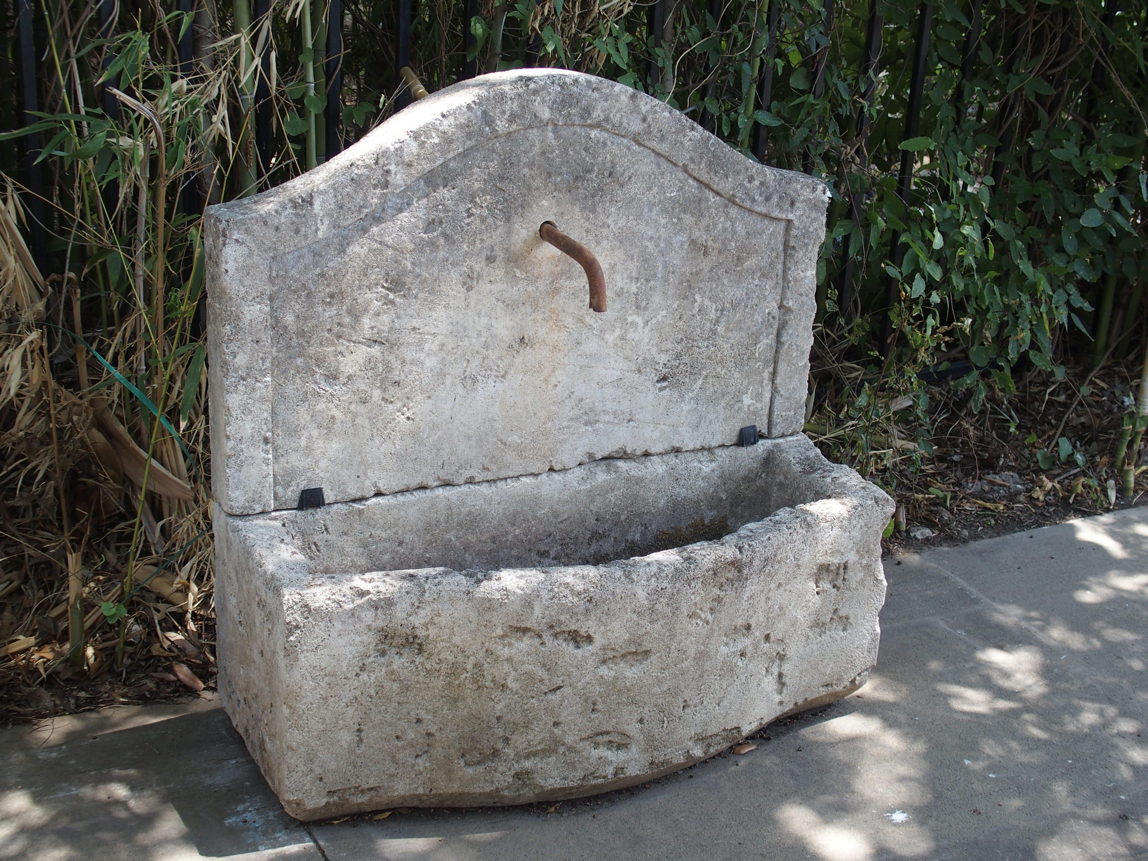 This small hand-carved, rustic wall fountain was made in France with local limestone and looks as if it is hundreds of years of old. The stone has spent several years in the elements, and it has a mixed color of greys, white, and black, that can