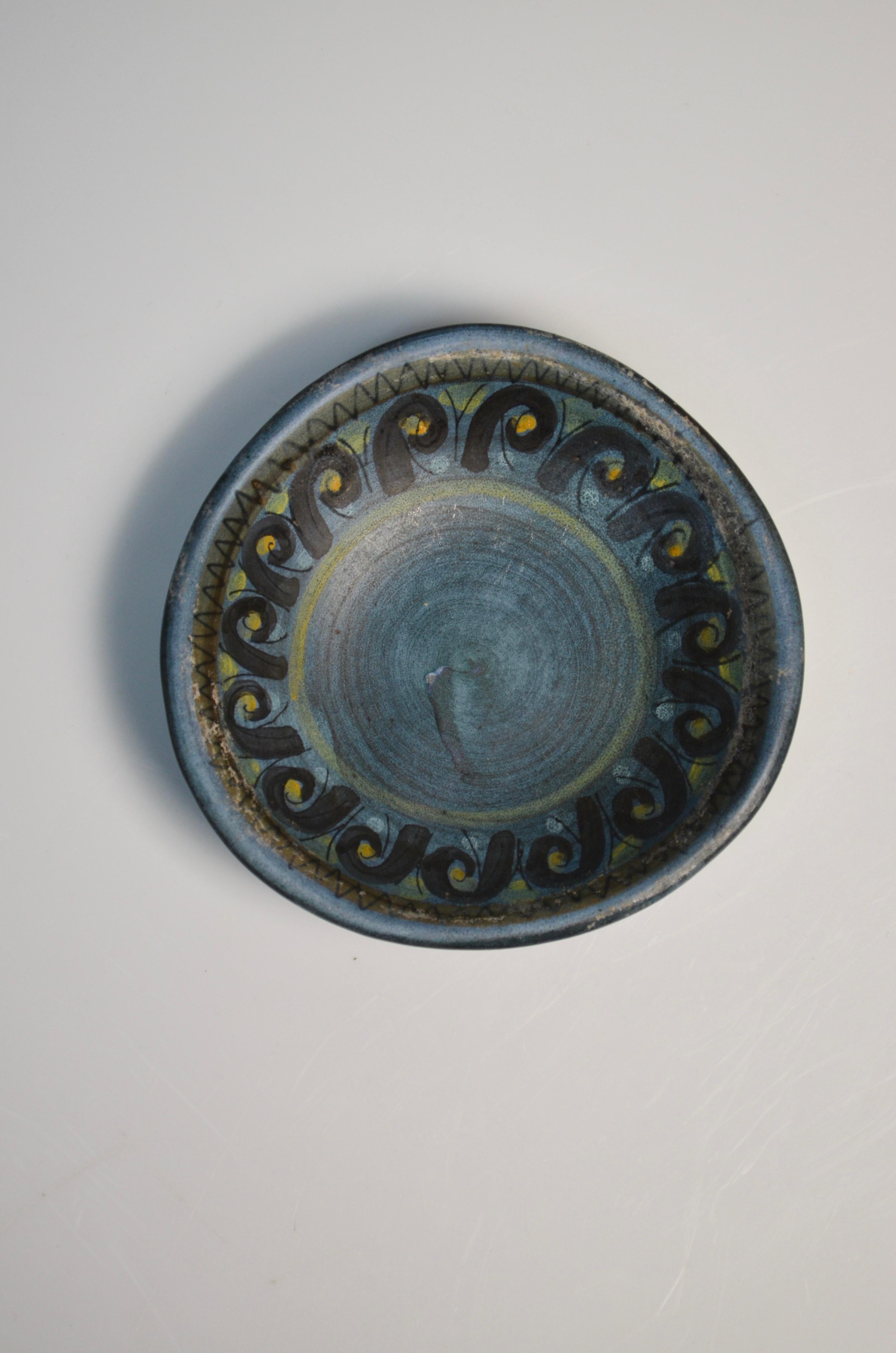Incantevole piccolo piatto in ceramica di Jean De Lespinasse, una figura di spicco della ceramica francese del XX secolo. Questo pezzo presenta un bellissimo disegno dipinto a mano nei toni del blu, del nero e del giallo, con motivi geometrici e a
